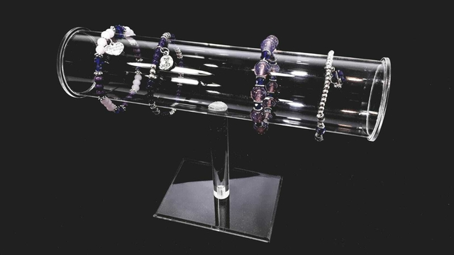 Expositor de pulseras de acrílico transparente con varias pulseras sobre fondo negro.