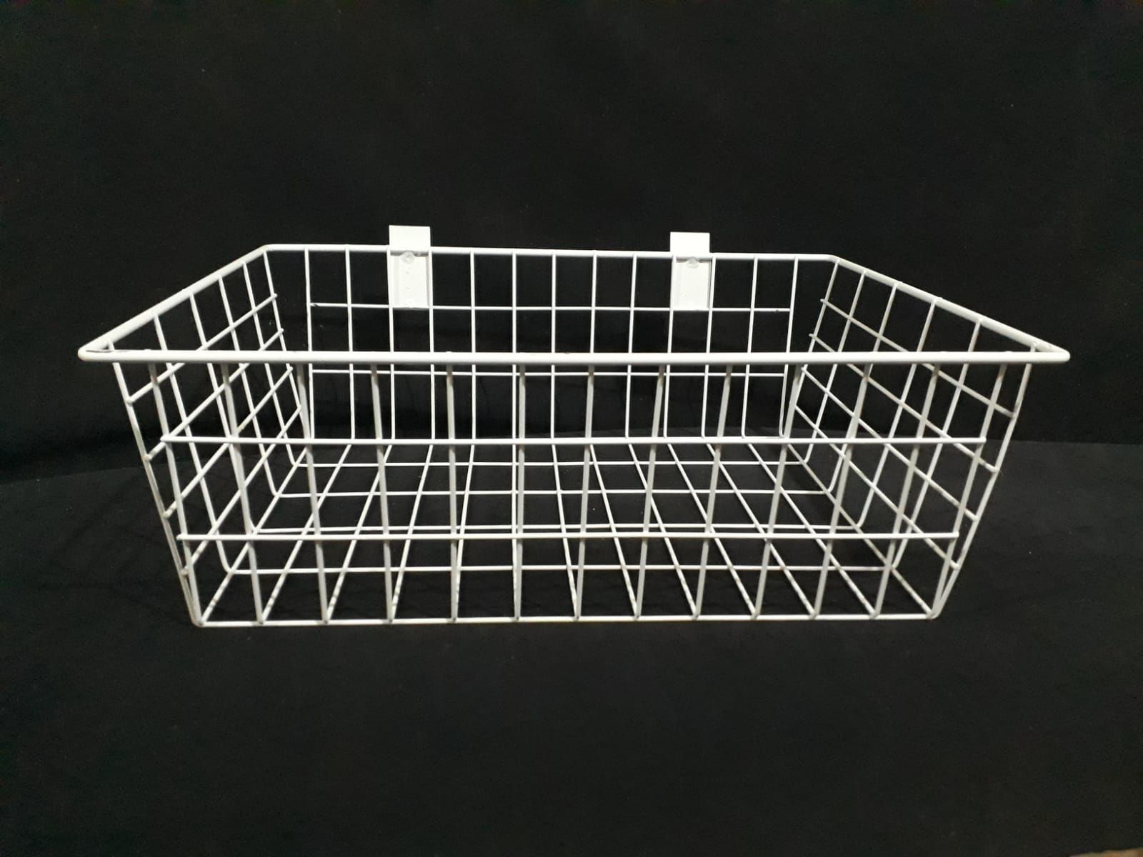 Cesta de alambre blanca con dos pinzas para colgar, sobre fondo negro.