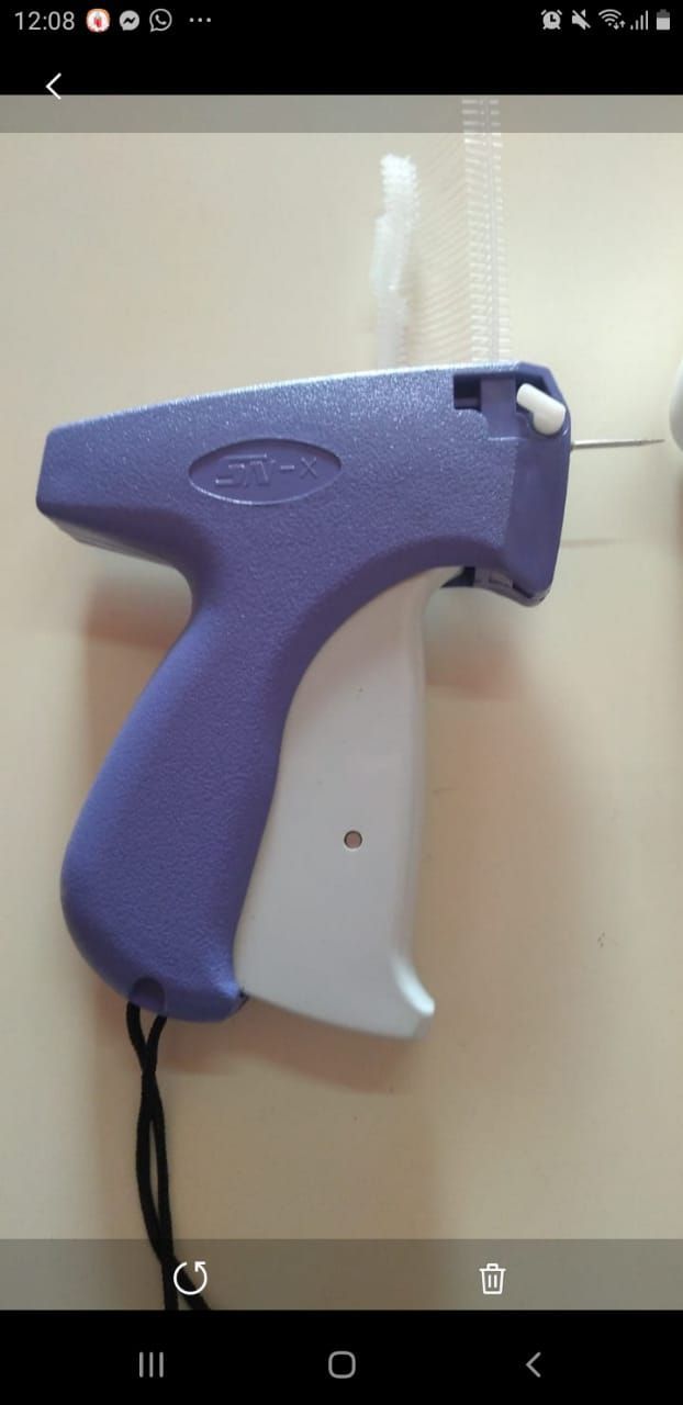 Pistola etiquetadora de prendas de color morado y blanco colgada en una pared de color claro.