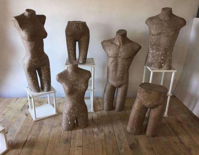 Maniquíes en tonos neutros sobre suelo de madera, algunos sobre soportes blancos.