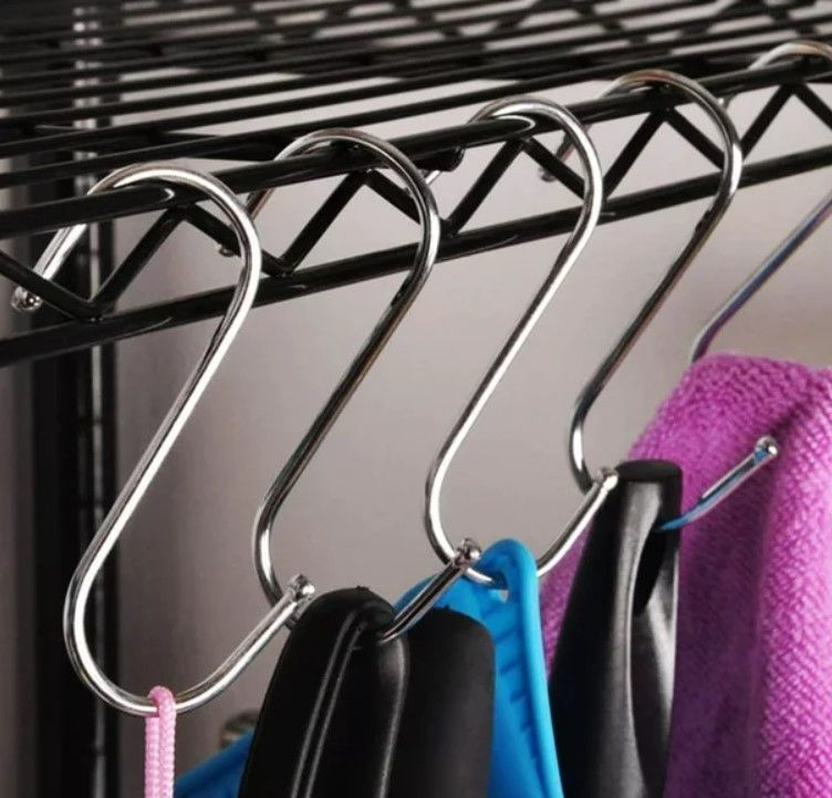 Ganchos en forma de S que cuelgan de un estante de alambre negro y que sostienen artículos como toallas y bolsos.