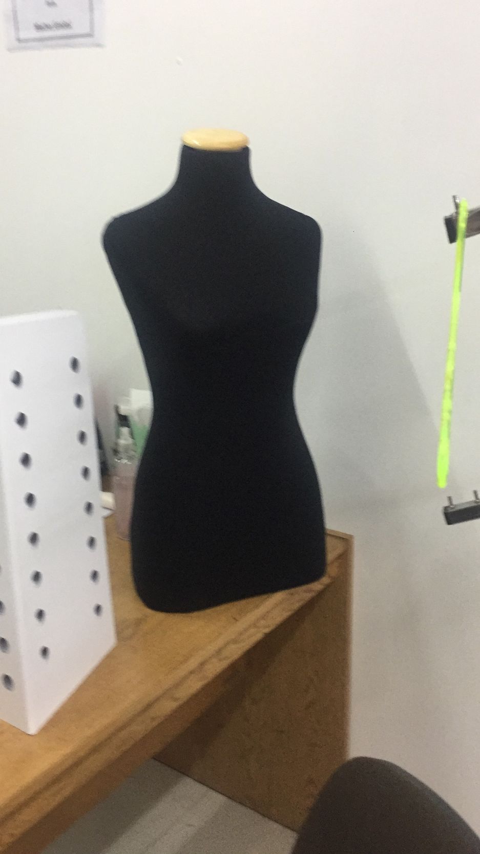 Maniquí de color negro sobre un escritorio de madera, junto a un objeto blanco con puntos negros y una correa verde colgante.