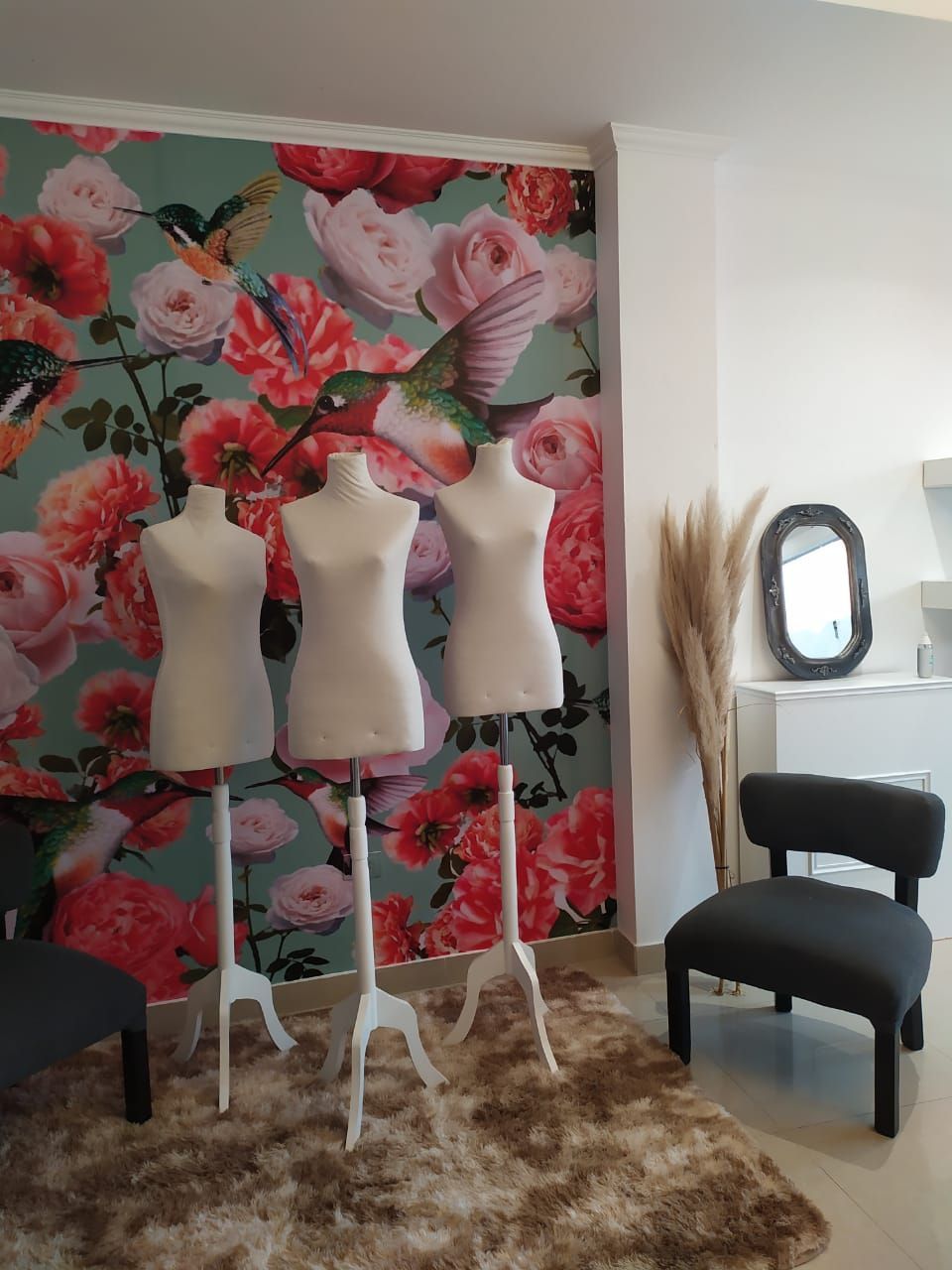 Tres siluetas de modista delante de un papel pintado floral, con una silla y un espejo en una habitación.