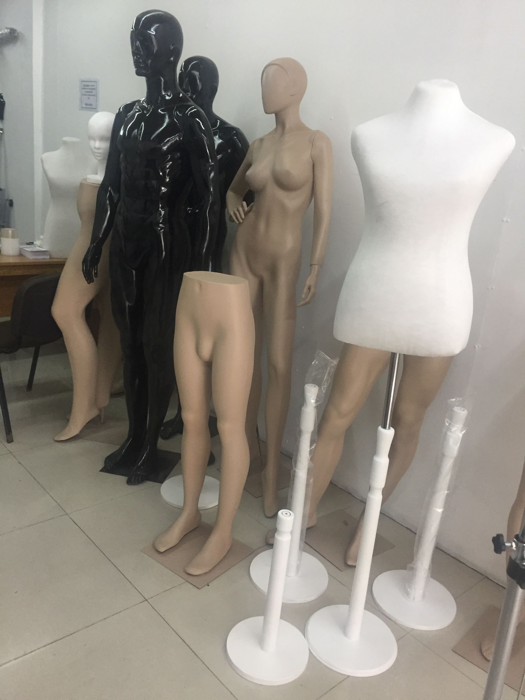 Maniquíes en una tienda, de varios estilos y colores, algunos con sólo piernas, exhibidos en soportes.