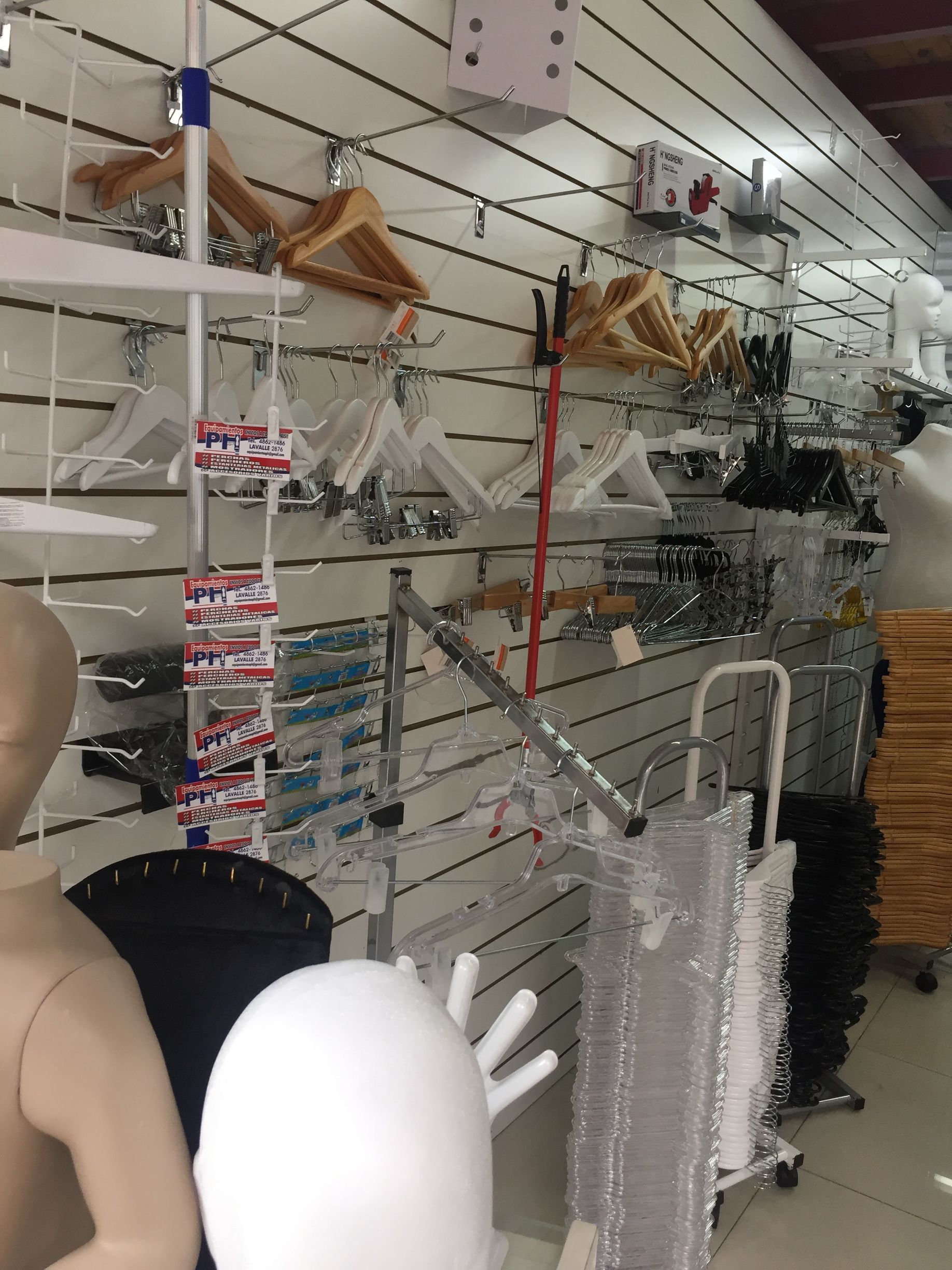 Exhibición de perchas de ropa, maniquíes y suministros minoristas en una pared de listones.