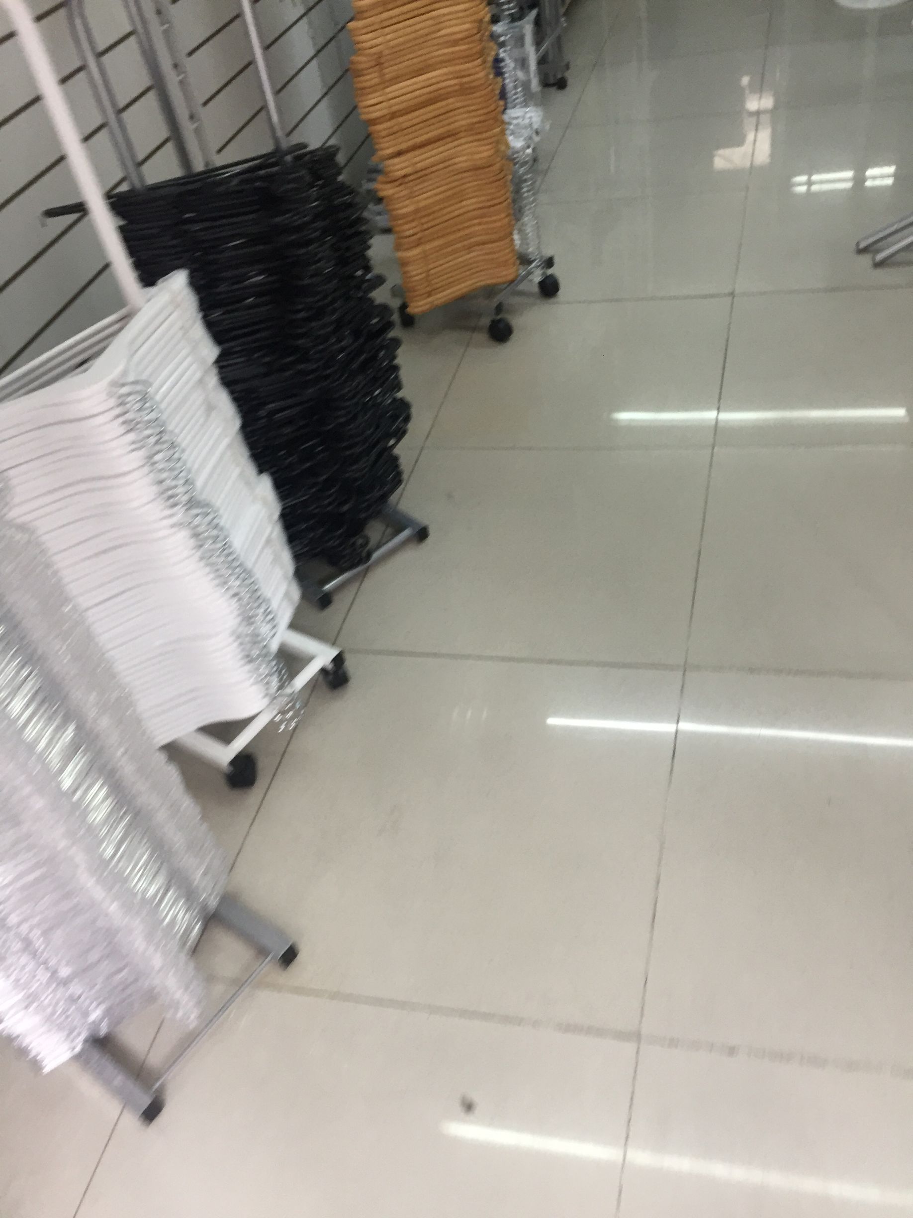 Filas de perchas de ropa apiladas en estantes con ruedas en una tienda, incluidas las de color blanco, negro y tostado.