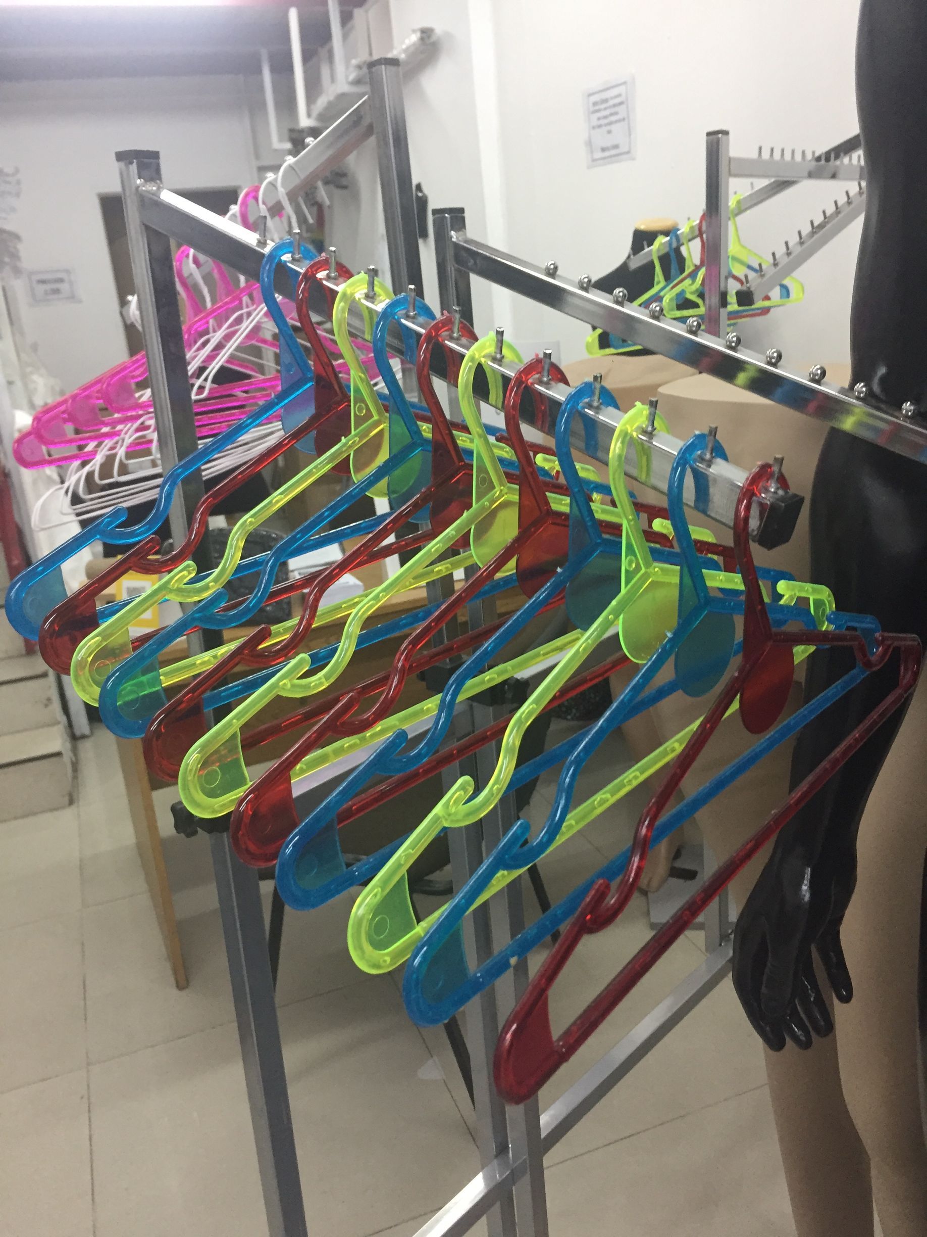 Perchas de ropa de plástico de colores en un estante de metal dentro de una tienda.