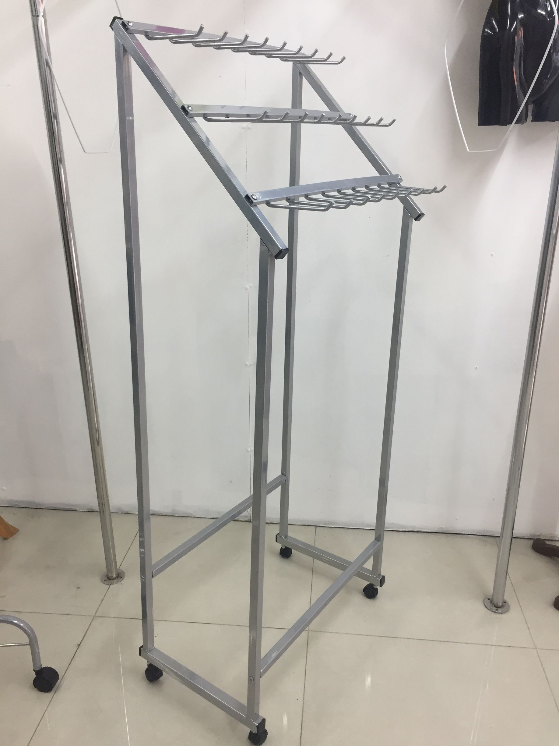 Perchero metálico con ruedas y múltiples niveles en ángulo para colgar ropa.