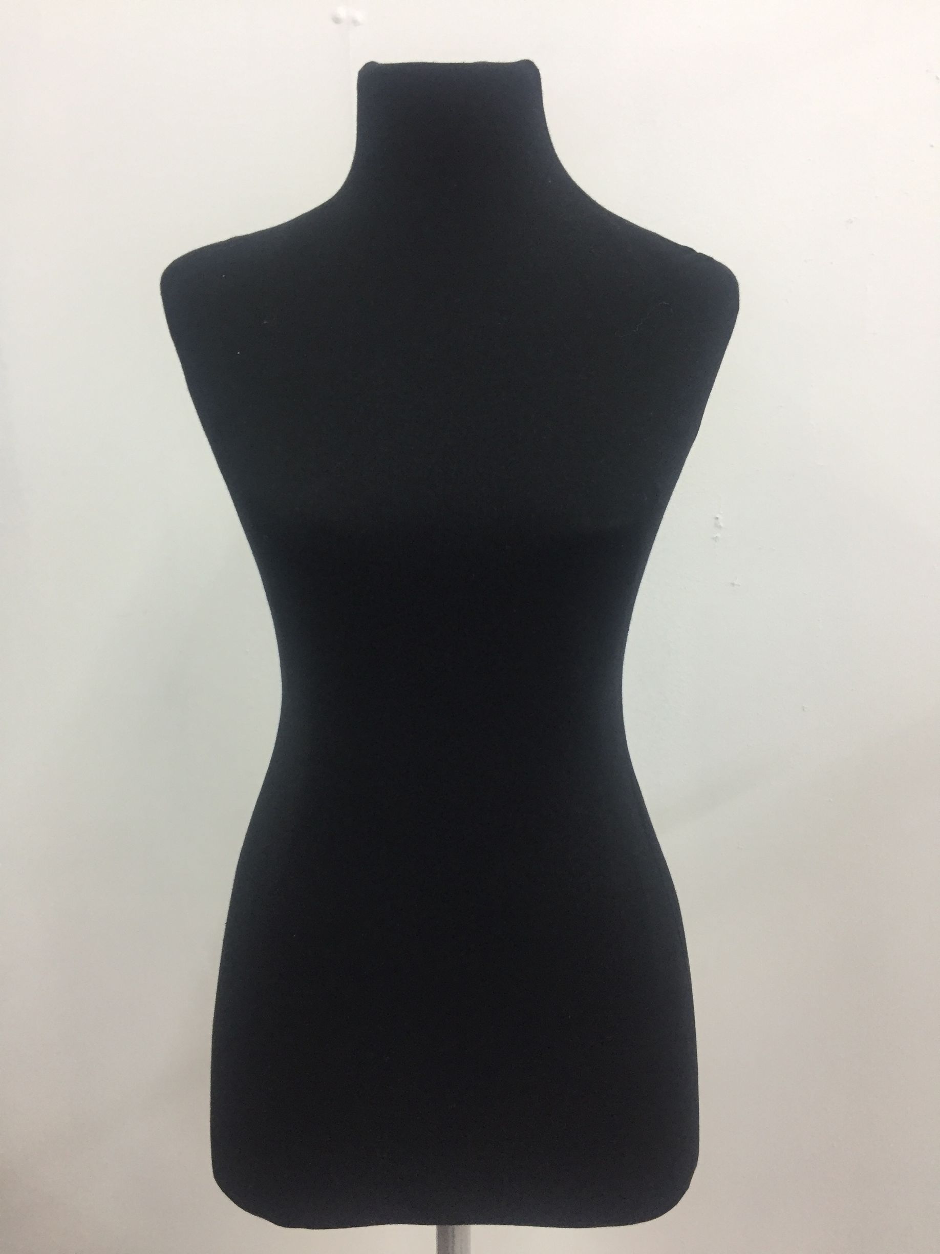 Maniquí de vestir negro sobre soporte plateado, contra una pared blanca.