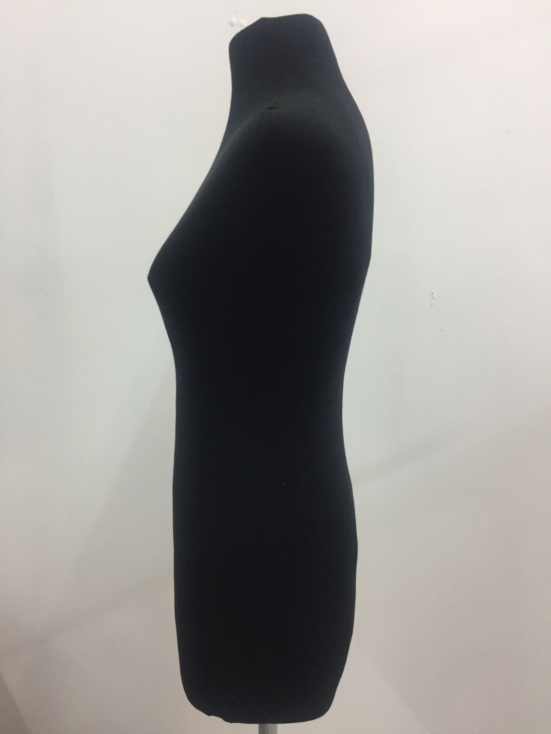 Maniquí de vestir de color negro, vista lateral, sobre un soporte contra una pared blanca.