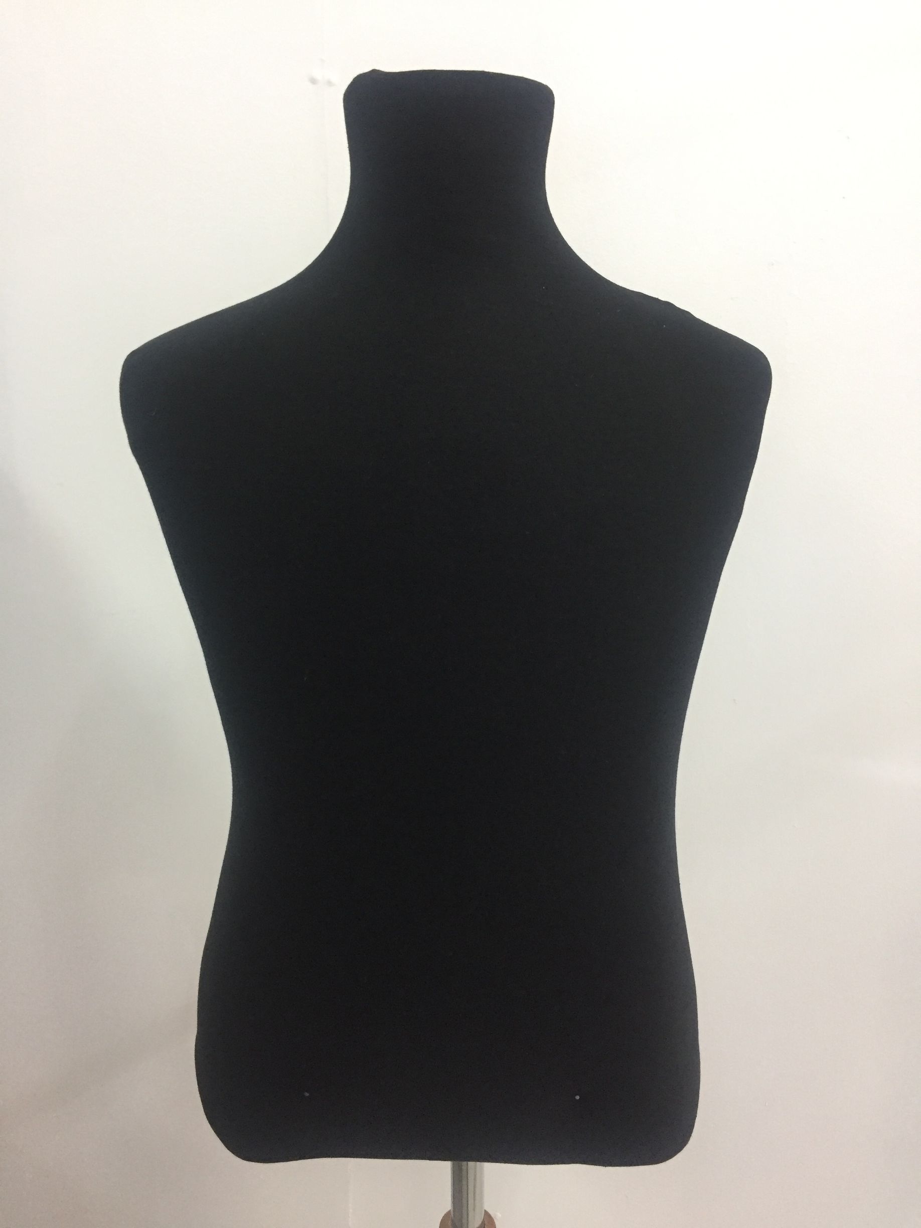 Maniquí de tela negra sobre soporte, contra una pared blanca.