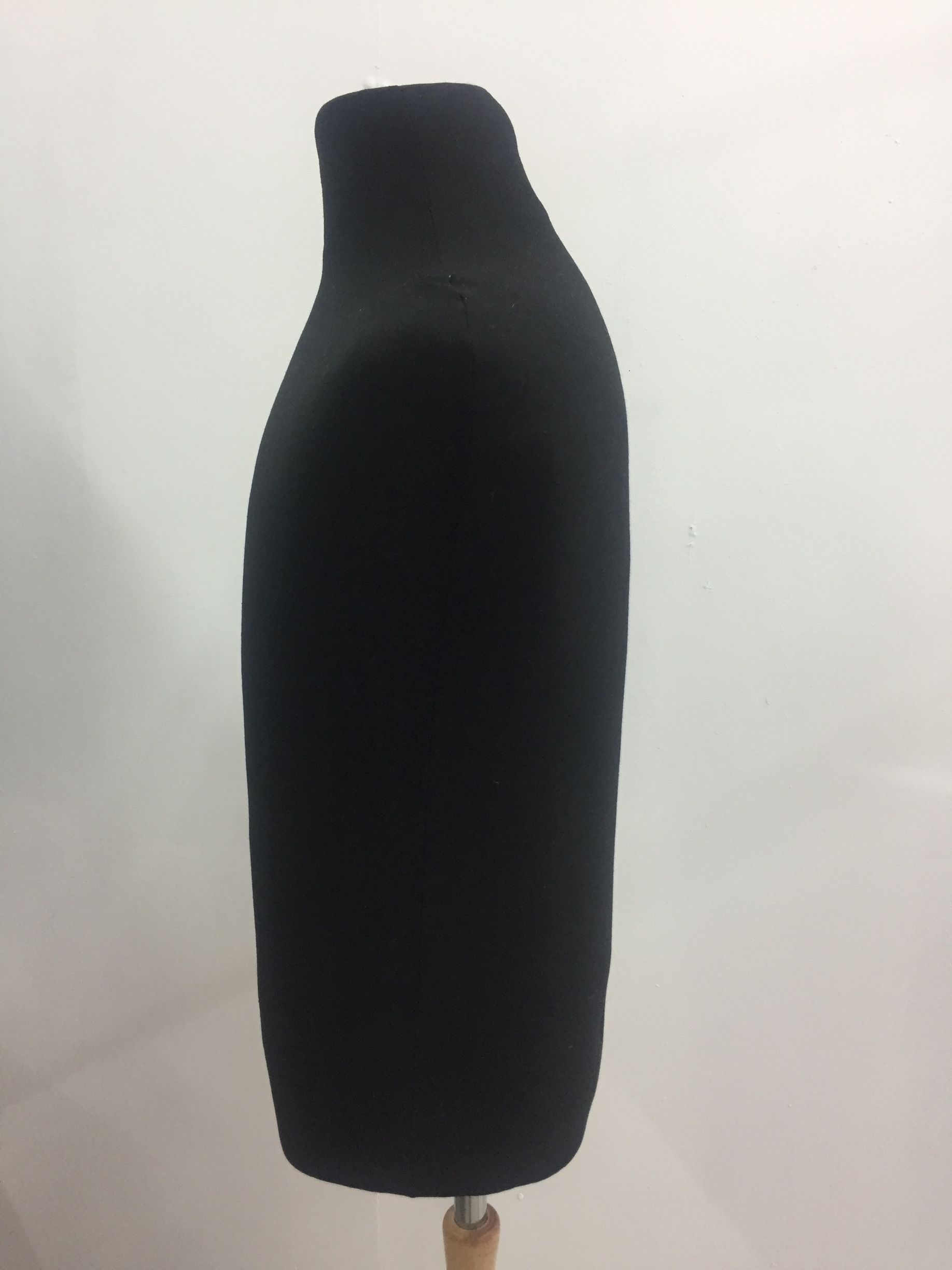 Maniquí de torso negro sobre soporte de madera sobre fondo blanco.