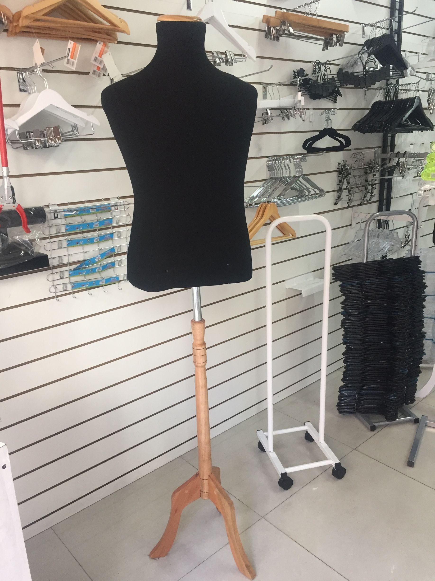 Maniquí de torso negro sobre un soporte de madera en una tienda, con perchas y otros expositores de ropa.