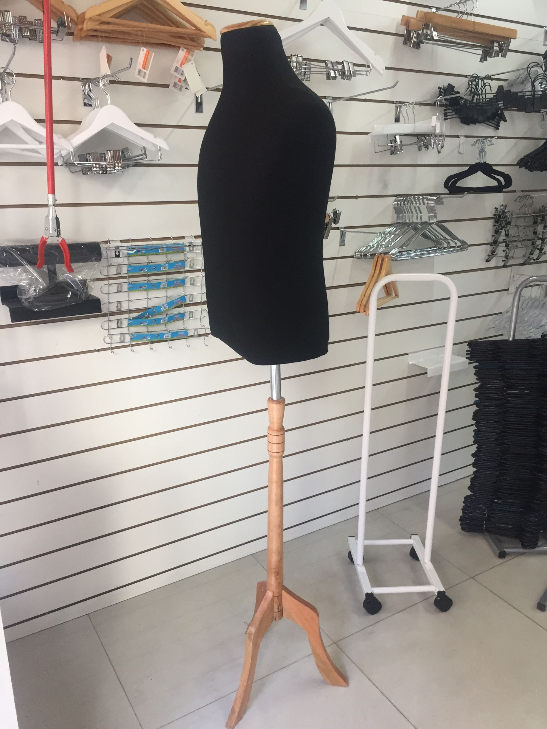 Maniquí de torso negro sobre soporte de madera, dentro de una tienda con perchas en la pared.
