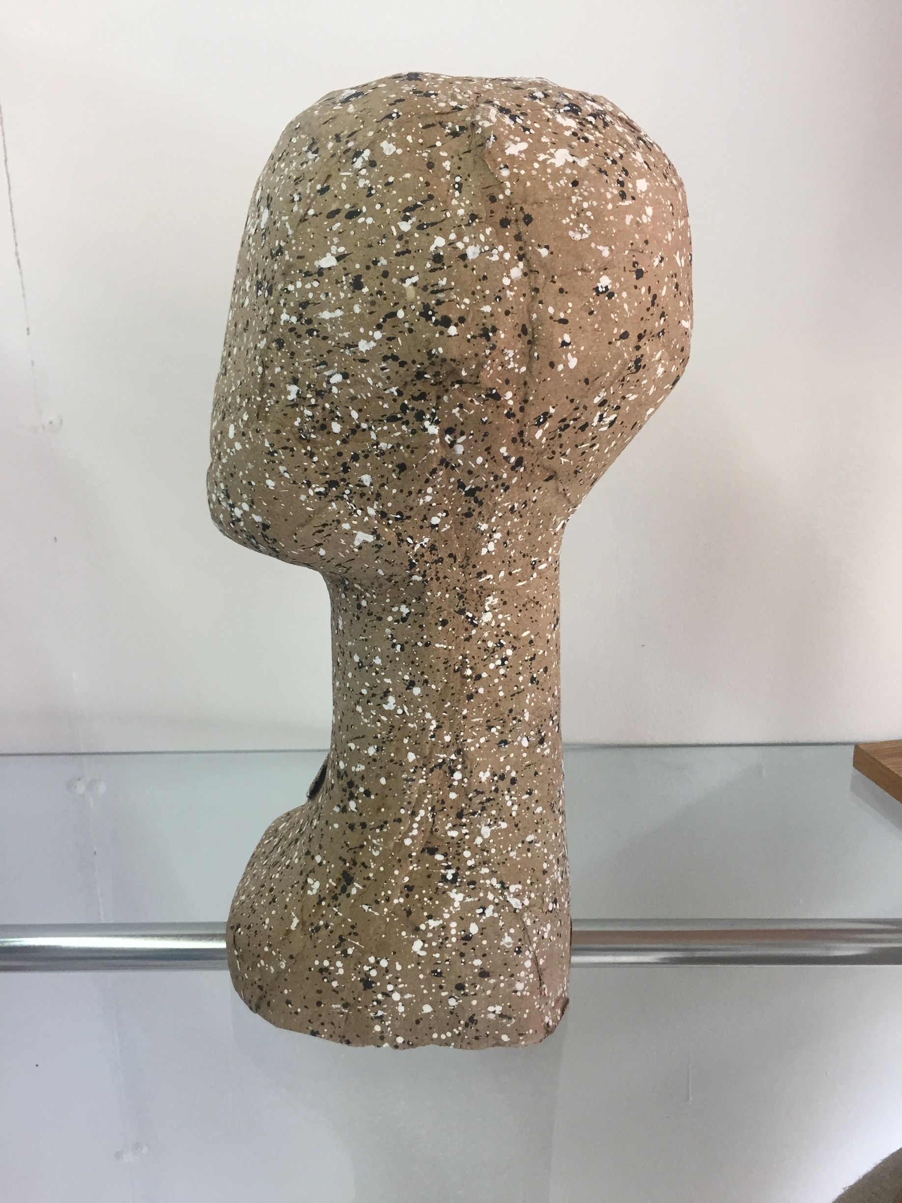 Cabeza de maniquí con textura moteada de color marrón; expuesta en un estante.