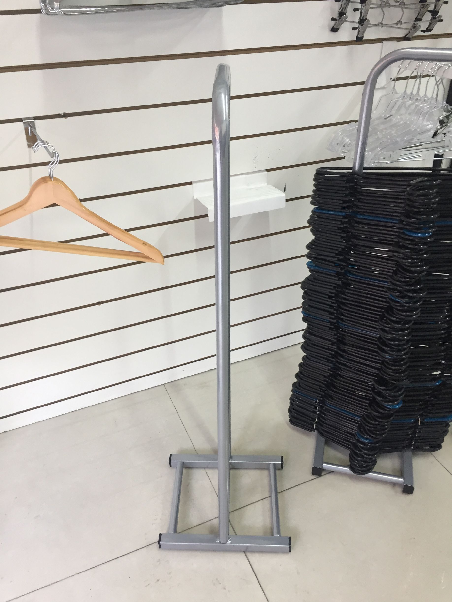 Perchero plateado en un establecimiento minorista, con perchas y perchas negras apiladas visibles.