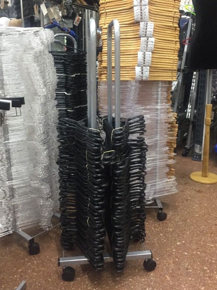 Pila de perchas negras en un estante con ruedas en una tienda, con cajas de cartón en el fondo.