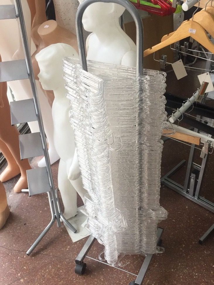 Estante de exhibición con perchas de plástico transparente, cerca de maniquíes infantiles.