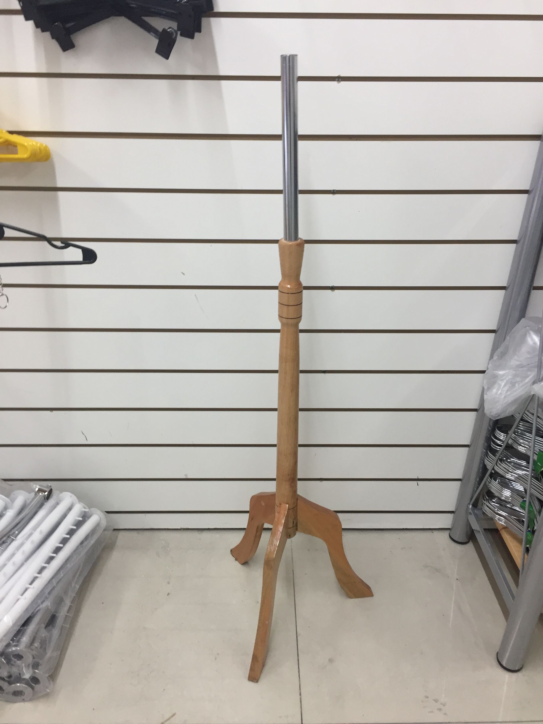 Maniquí de madera con poste de metal, apoyado sobre una pared de listones blancos.