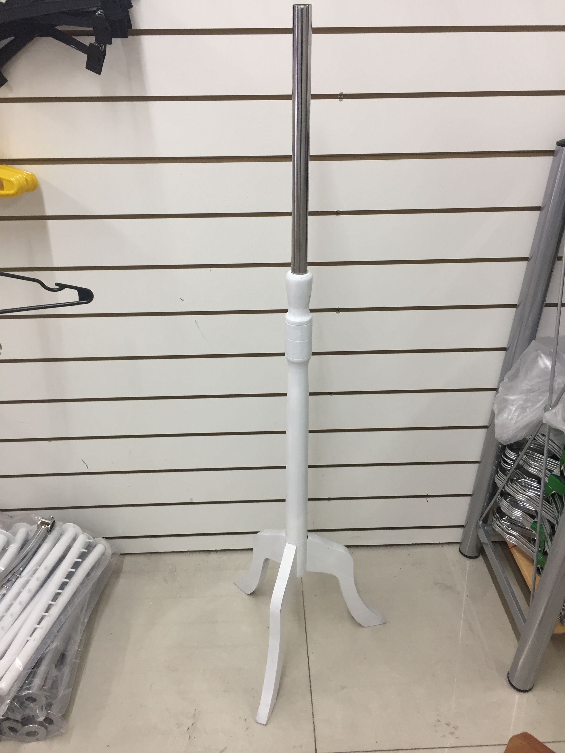 Expositor de ropa de color blanco, con poste plateado, contra una pared con listones blancos.