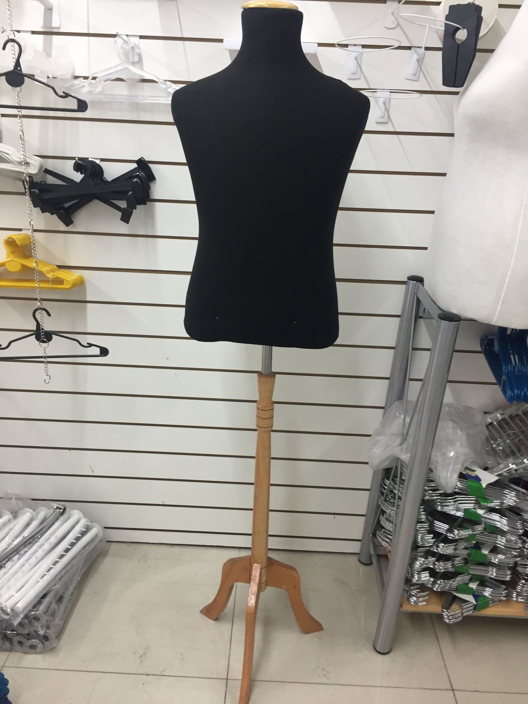 Maniquí de torso negro sobre soporte de madera en una tienda, con perchas y mercadería.