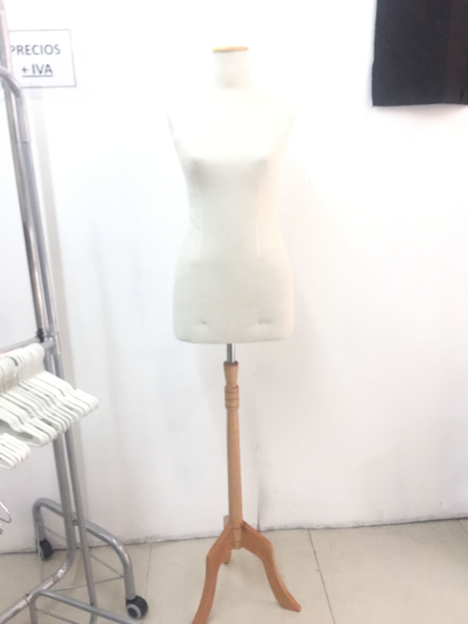 Un maniquí sobre un soporte de madera delante de una pared blanca y un perchero con ruedas.
