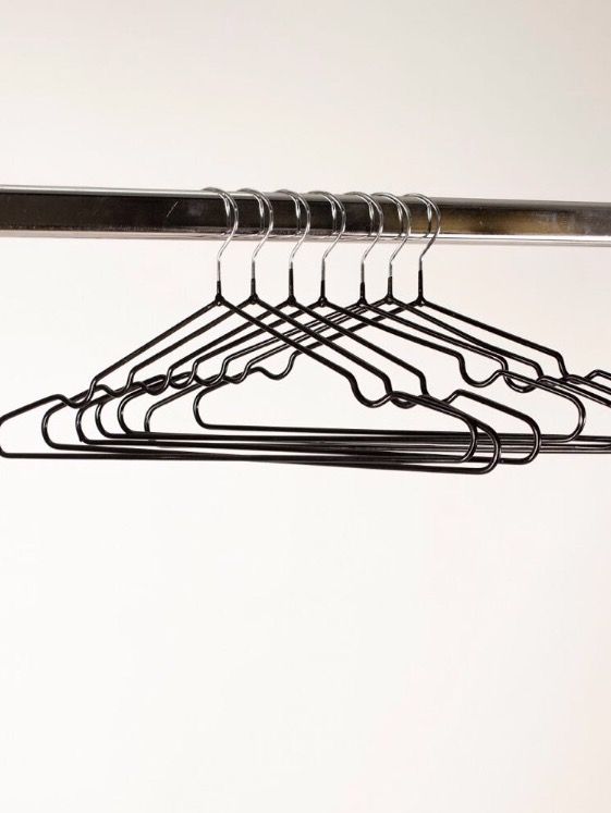 Perchas de alambre negras sobre una varilla de metal sobre un fondo blanco.