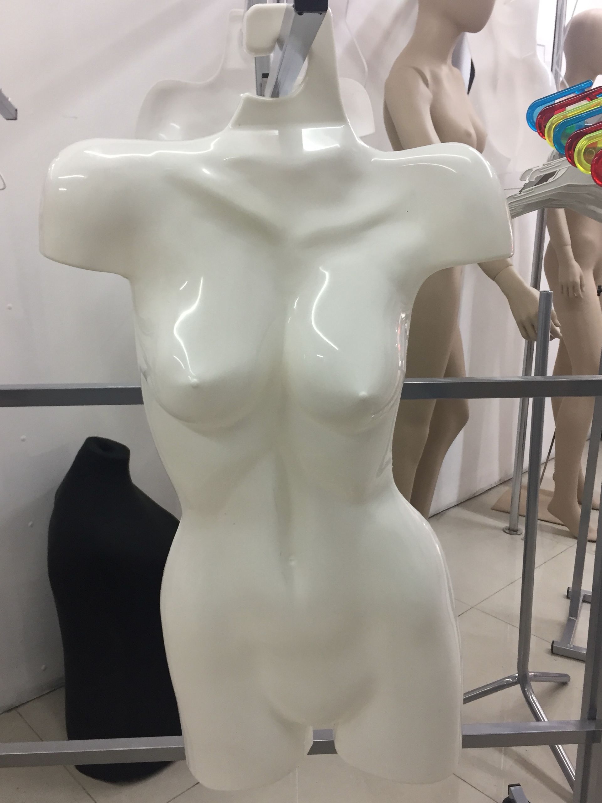 Maniquí de torso femenino de color blanco con percha adjunta, en un entorno de tienda.