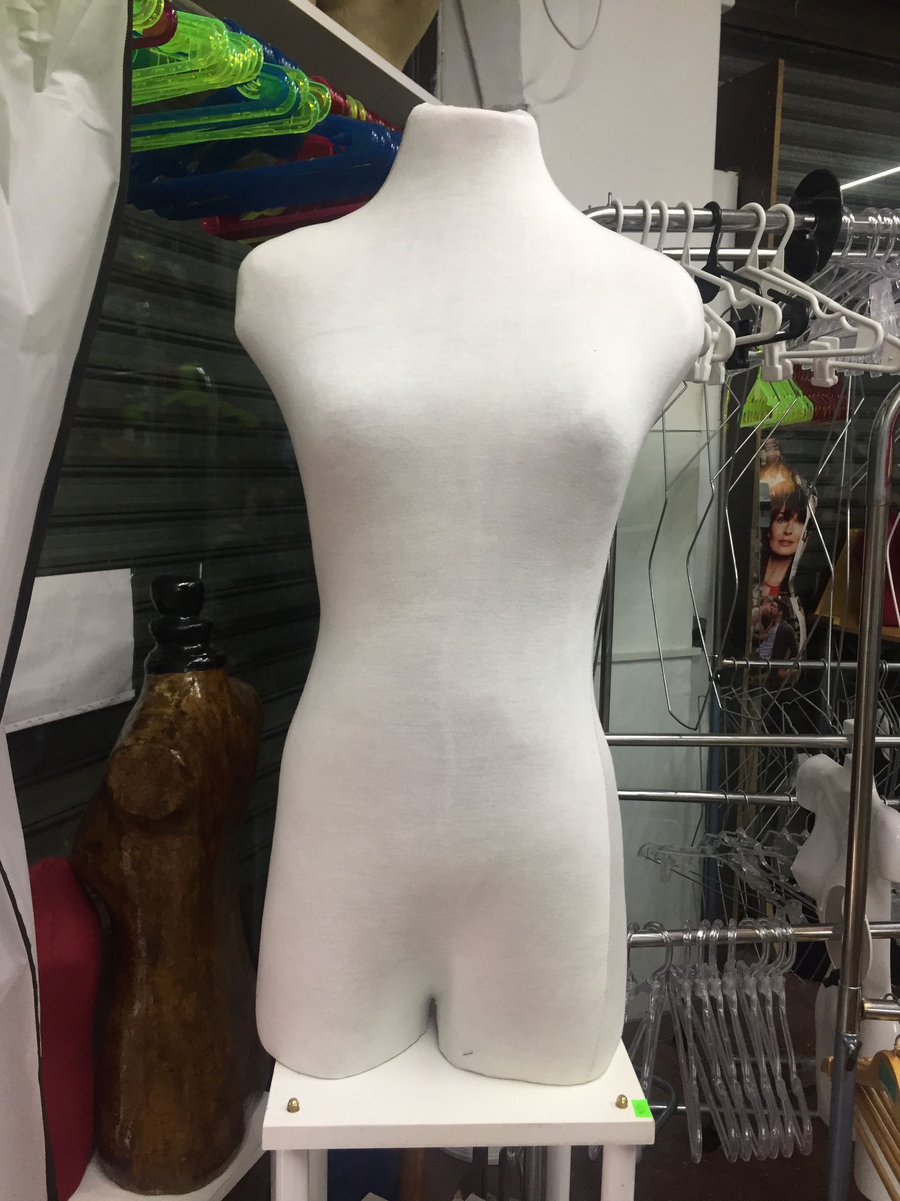 Torso de maniquí femenino de color blanco sobre un soporte blanco en una tienda de ropa.