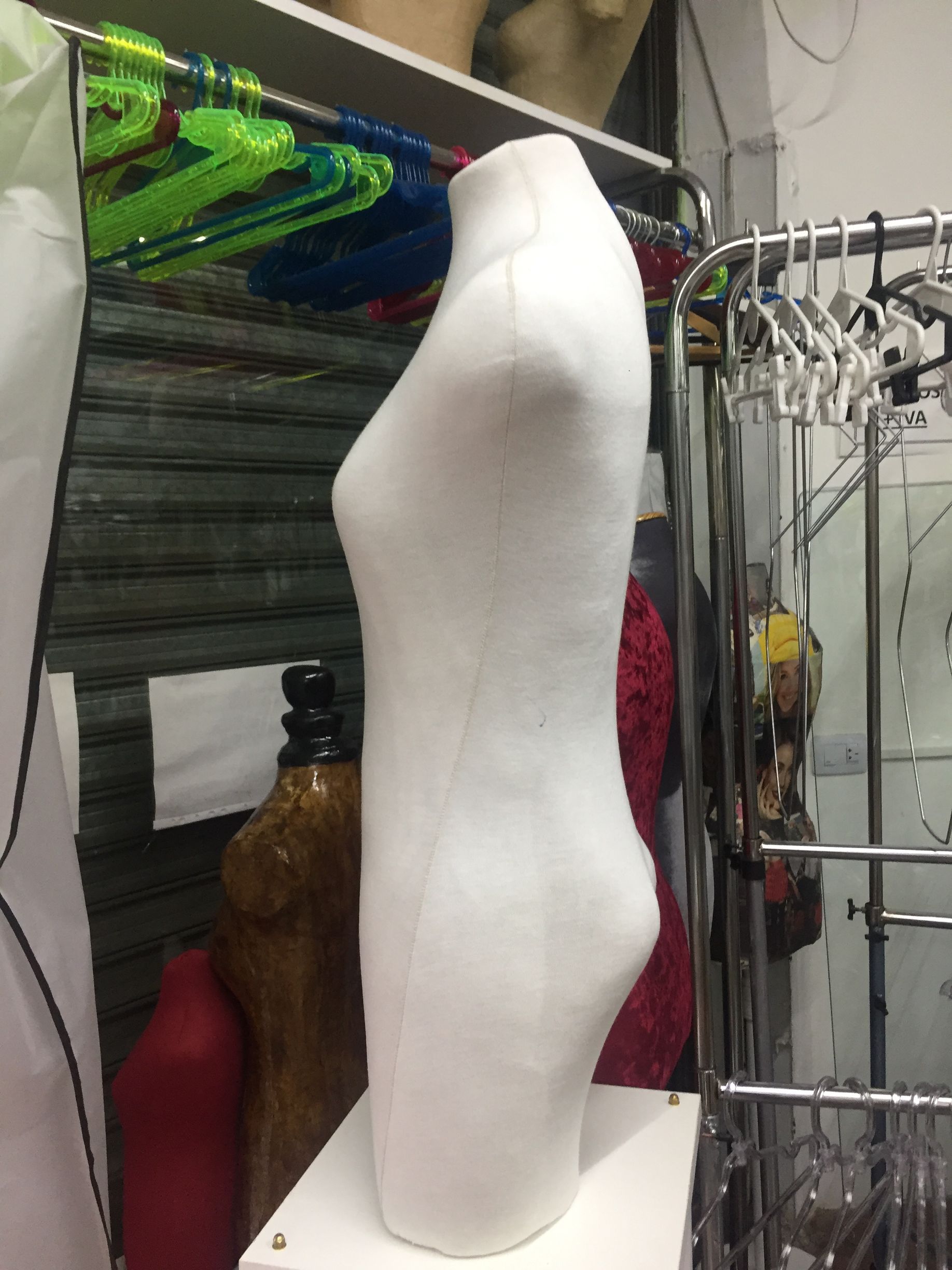 Maniquí de torso blanco en una tienda de ropa, junto a perchas y estantes de ropa.