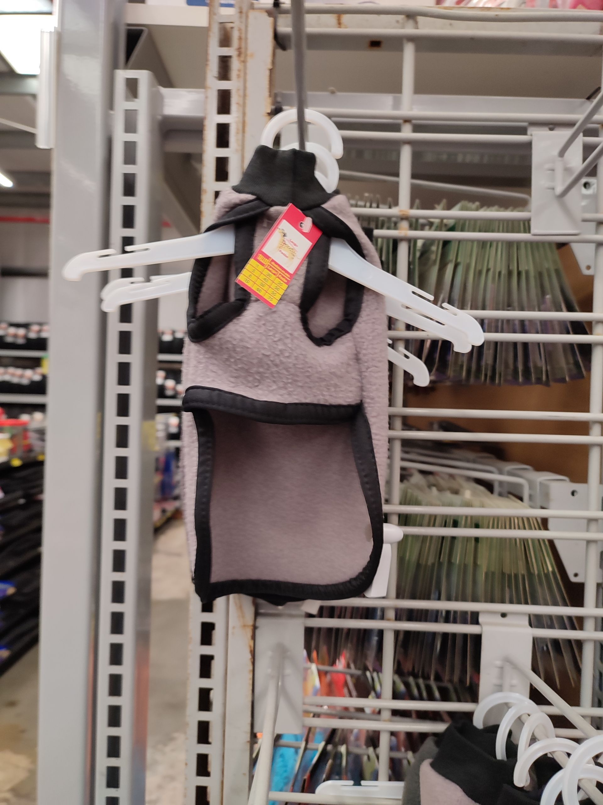 Chaleco para perro, gris con ribete negro, colgado en una percha blanca en una tienda.