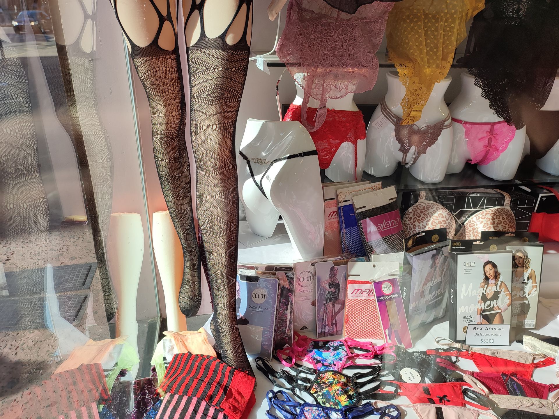 Exhibición de tienda de lencería con maniquíes que muestran medias estampadas, bragas y ropa interior empaquetada.