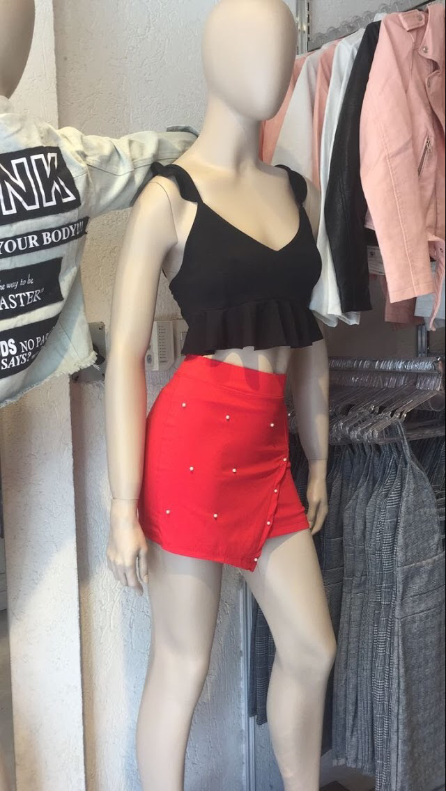 Maniquí con top negro y falda roja con pedrería, en un entorno de tienda de ropa.