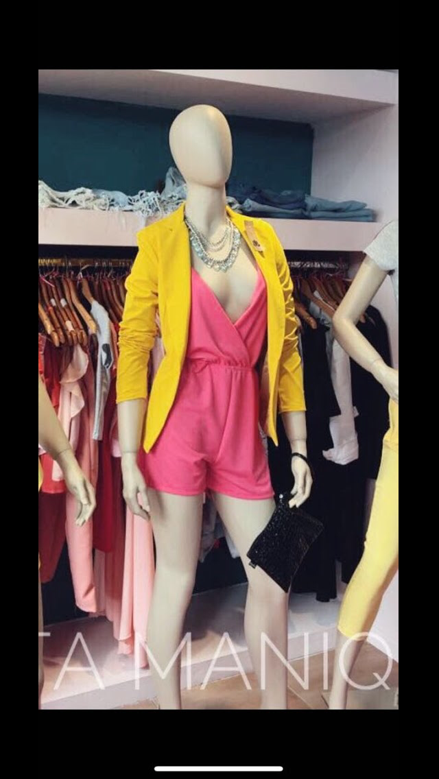 Maniquí con un mono rosa y un blazer amarillo en el escaparate de una tienda de ropa.