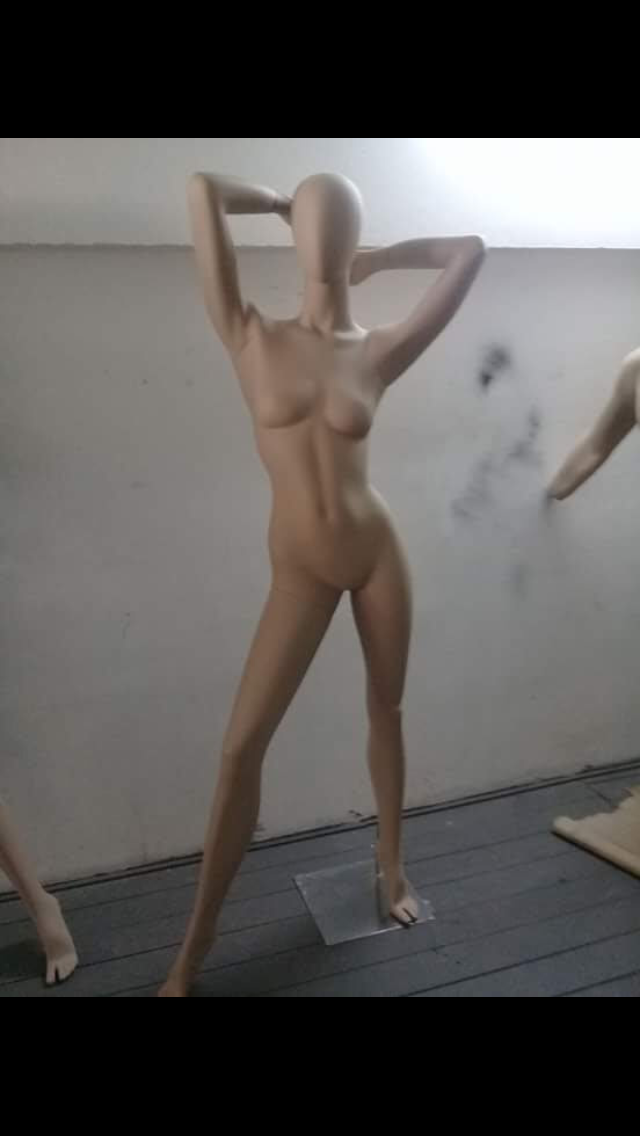 Maniquí con los brazos en alto, de pie en una habitación. Bronceado, sin rostro.