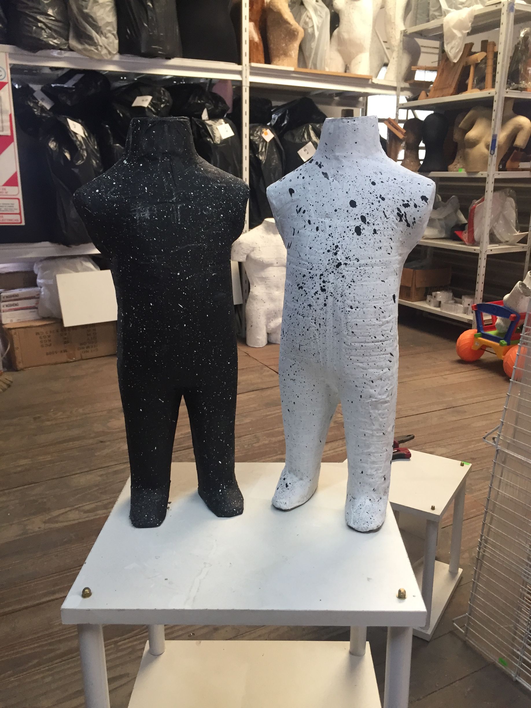Maniquíes de torso en blanco y negro con salpicaduras de pintura, de pie sobre una mesa blanca. Interior de tienda.