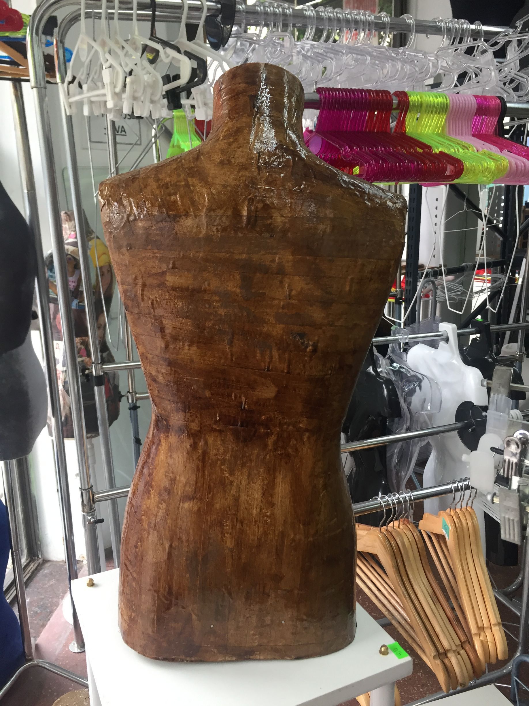 Vista posterior de un maniquí de torso de madera marrón en un estante blanco en una tienda.