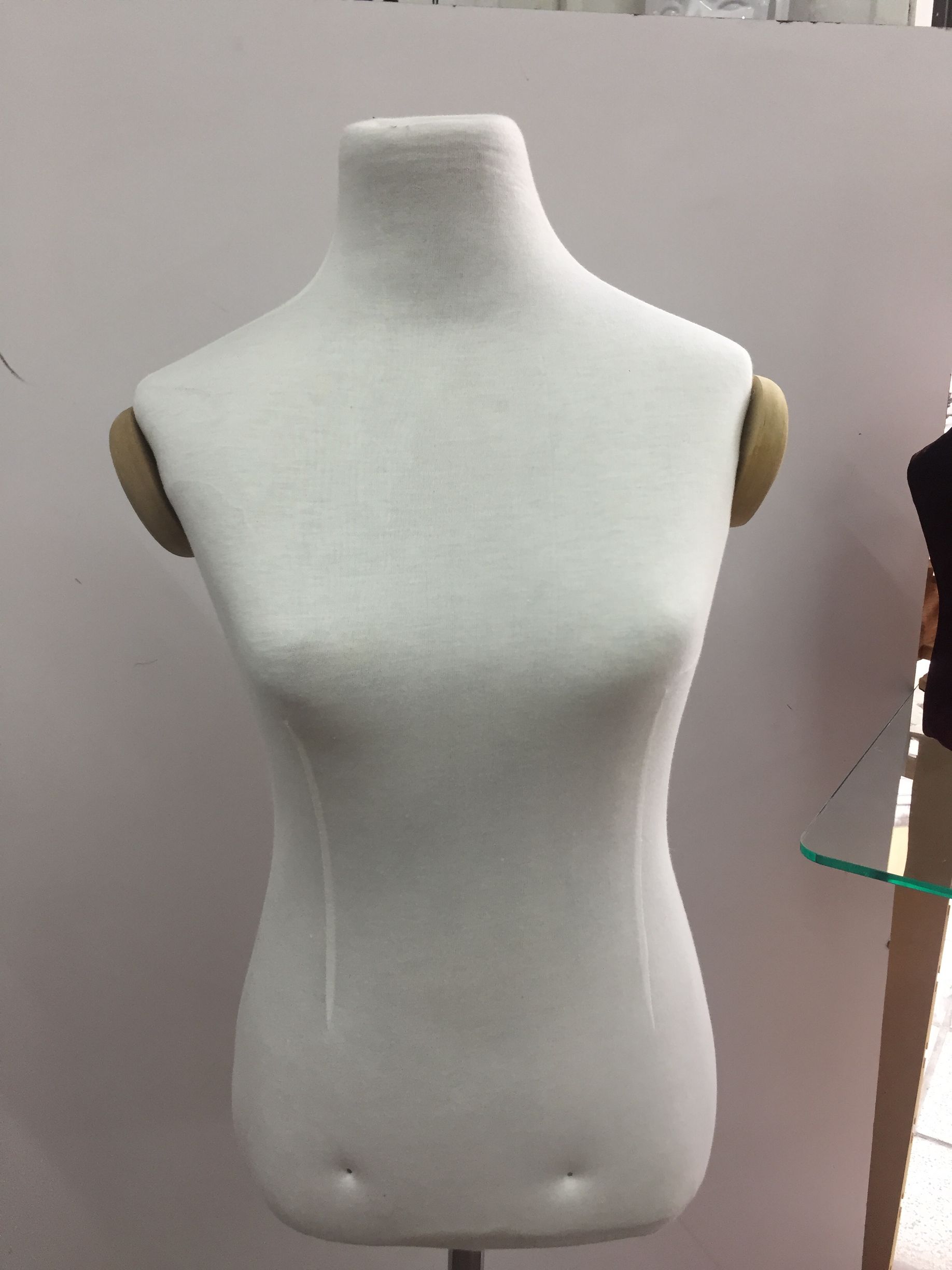 Torso de maniquí blanco con protectores de brazos de color canela, contra una pared lisa.