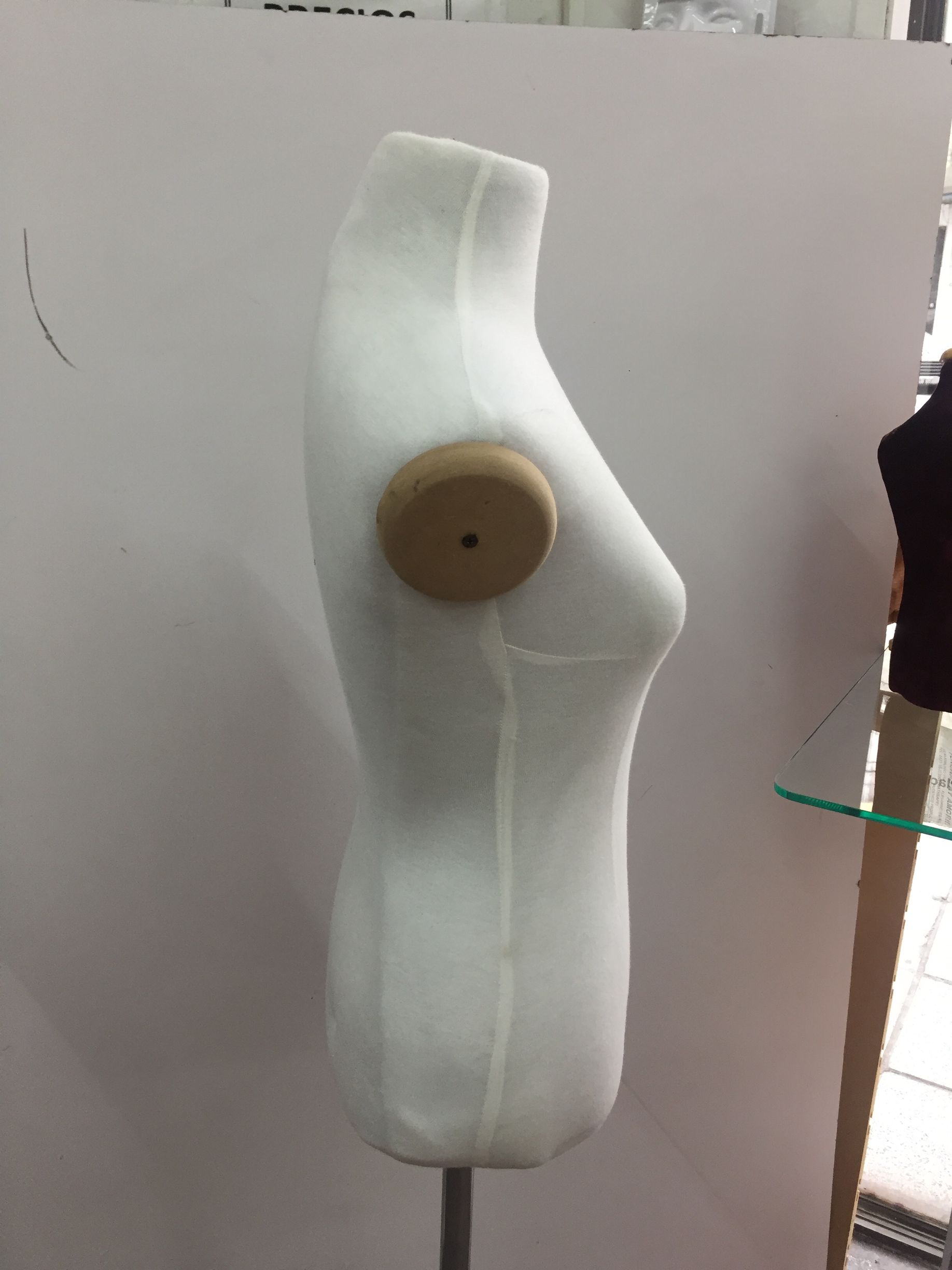 Forma de vestido con torso blanco, con una forma de pecho de madera adjunta, sobre un soporte de metal.