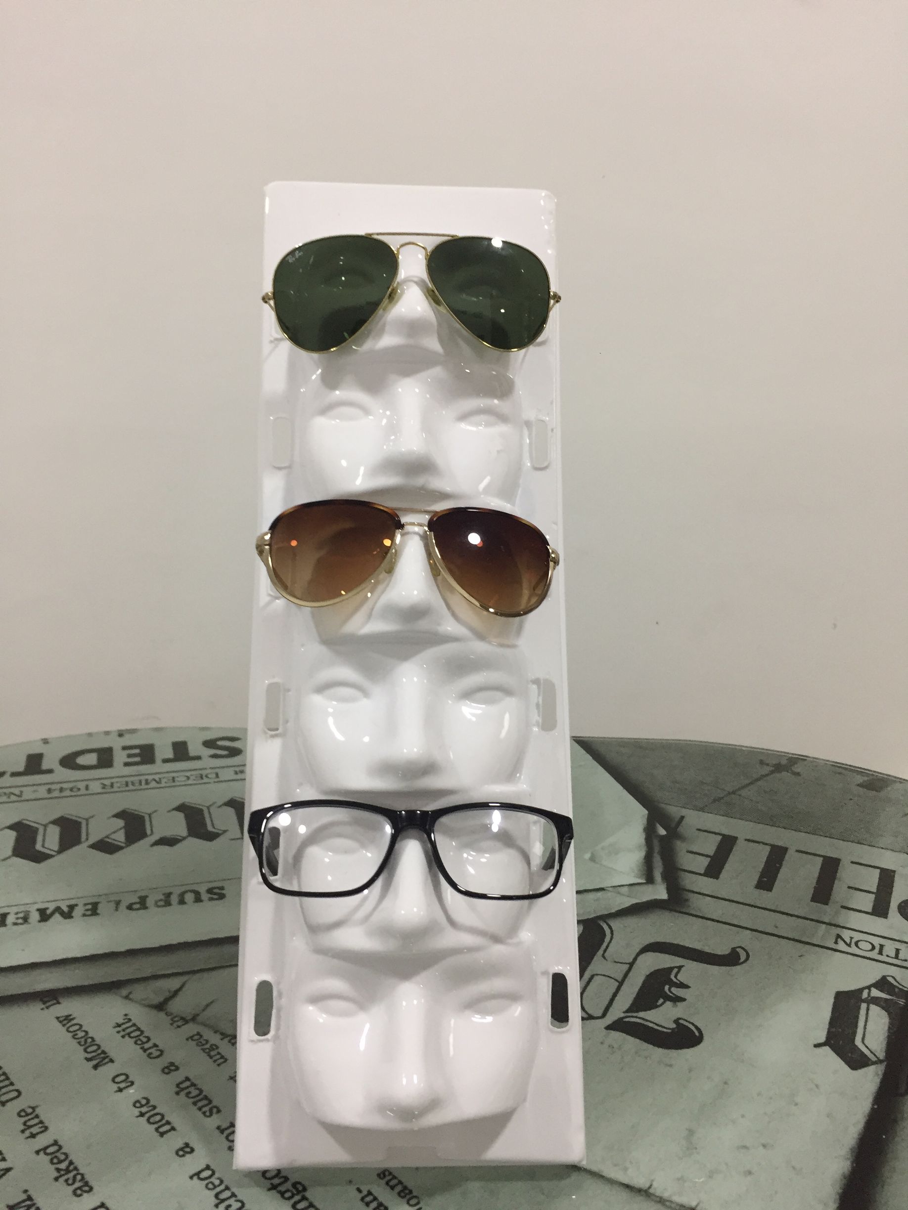 Gafas de sol exhibidas en un soporte para gafas blanco con forma de cara sobre un fondo neutro.