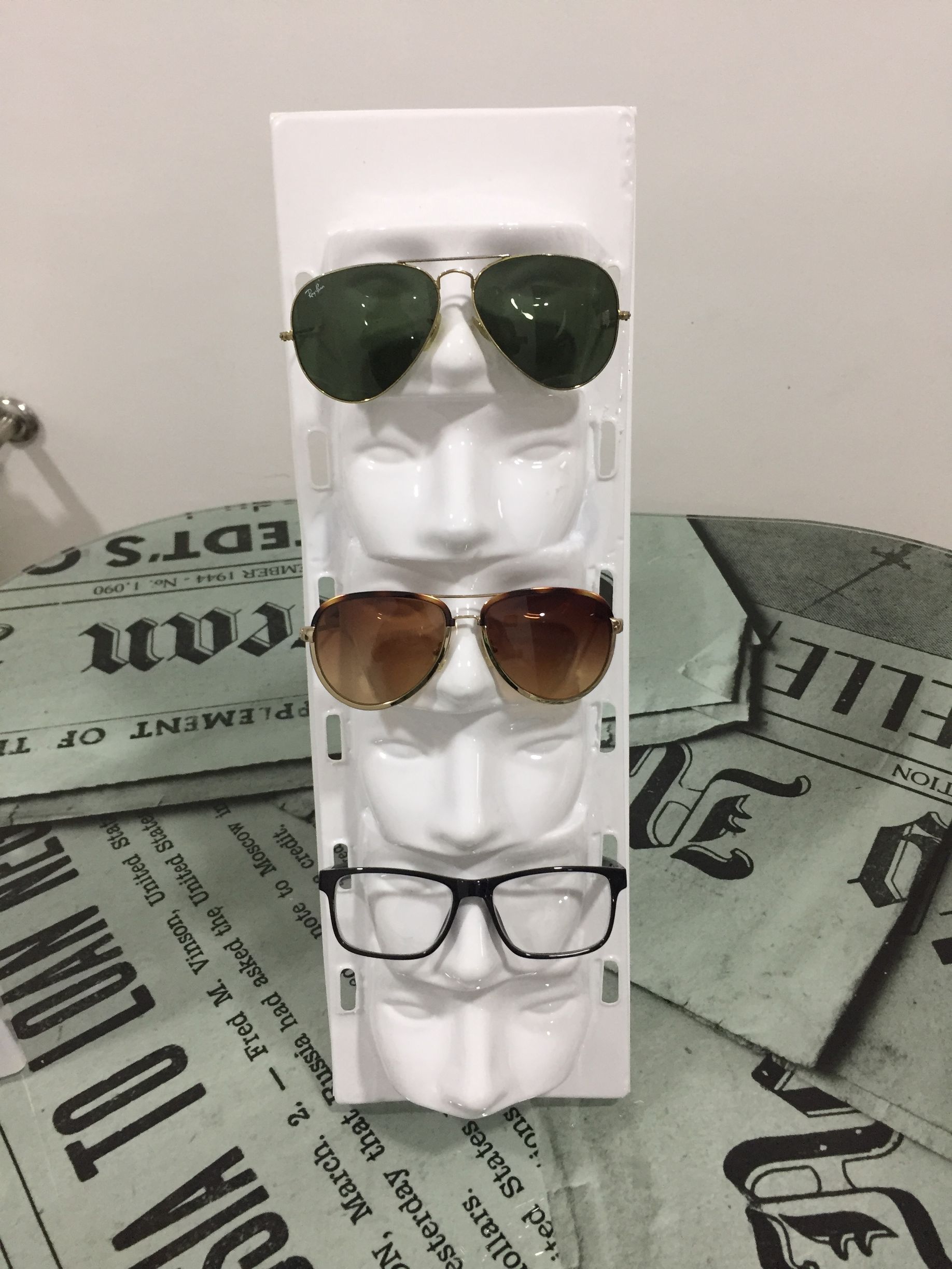 Expositor de gafas de sol con tres pares de gafas sobre formas blancas en forma de cabeza.