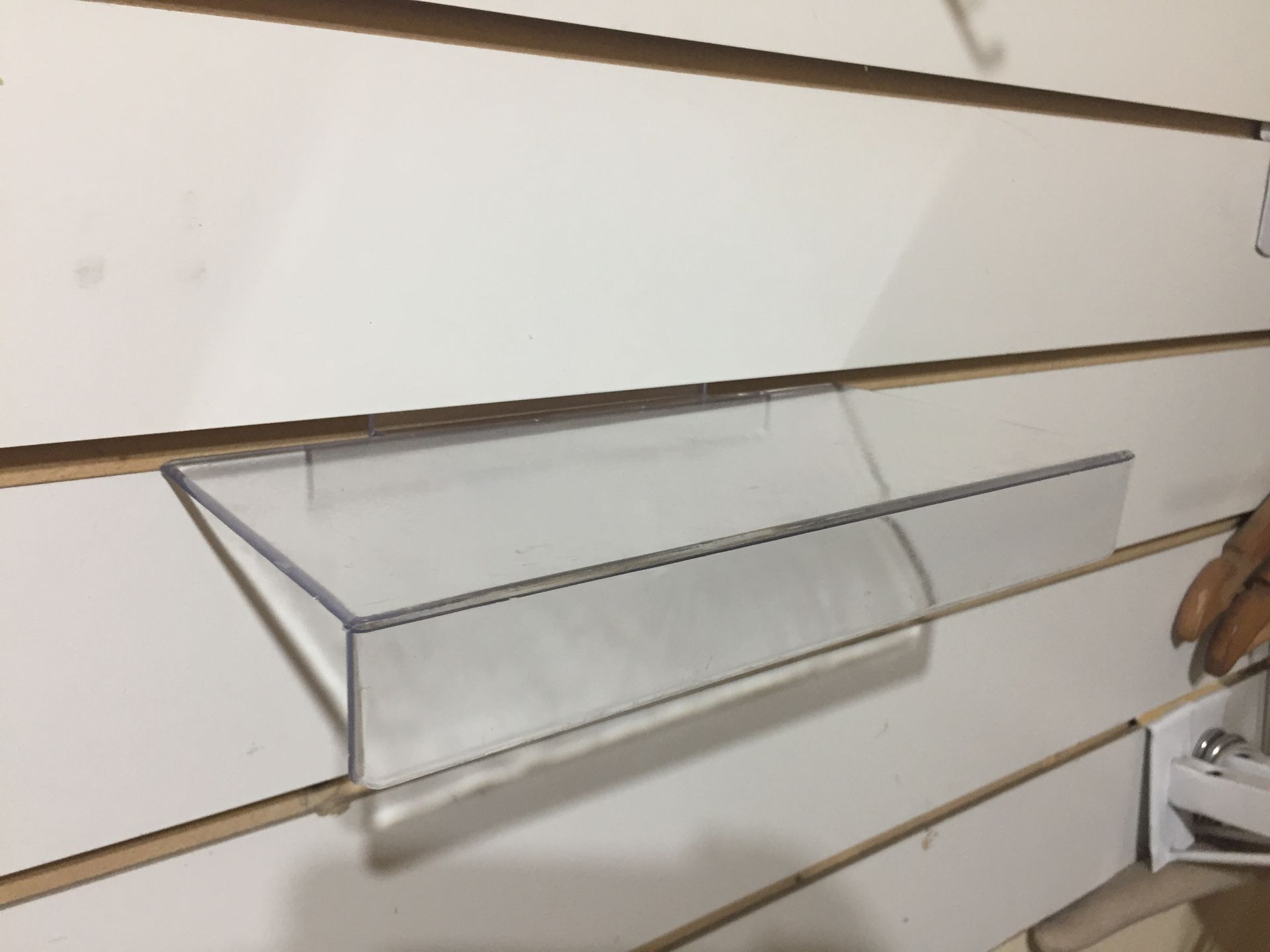 Estante de plástico transparente montado sobre una pared de listones de color blanco.