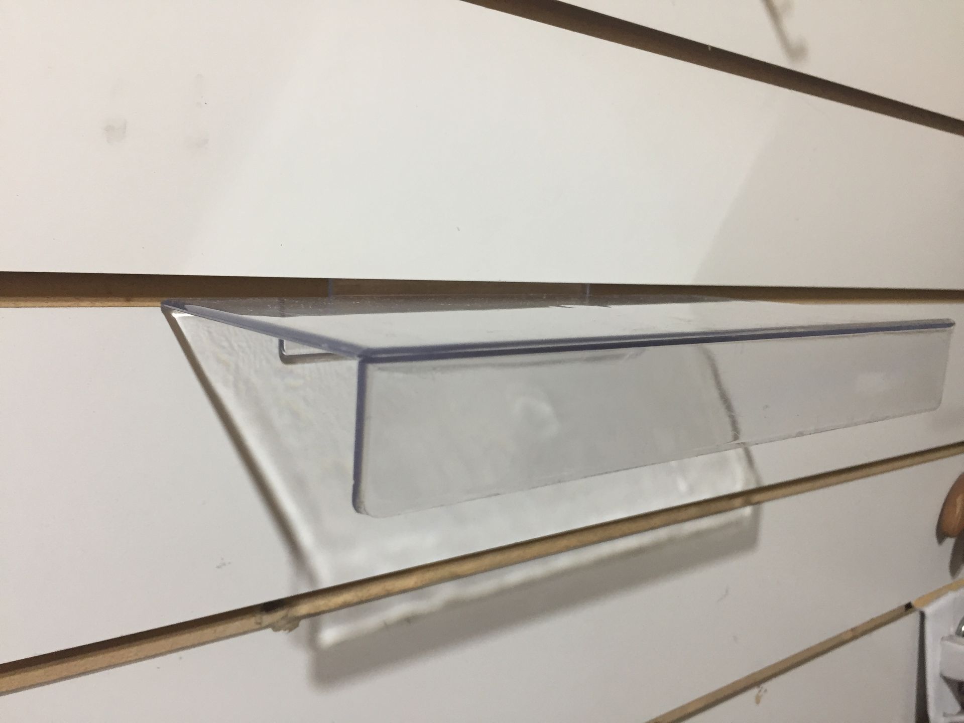 Estante de plástico transparente fijado a una pared ranurada de color blanco.