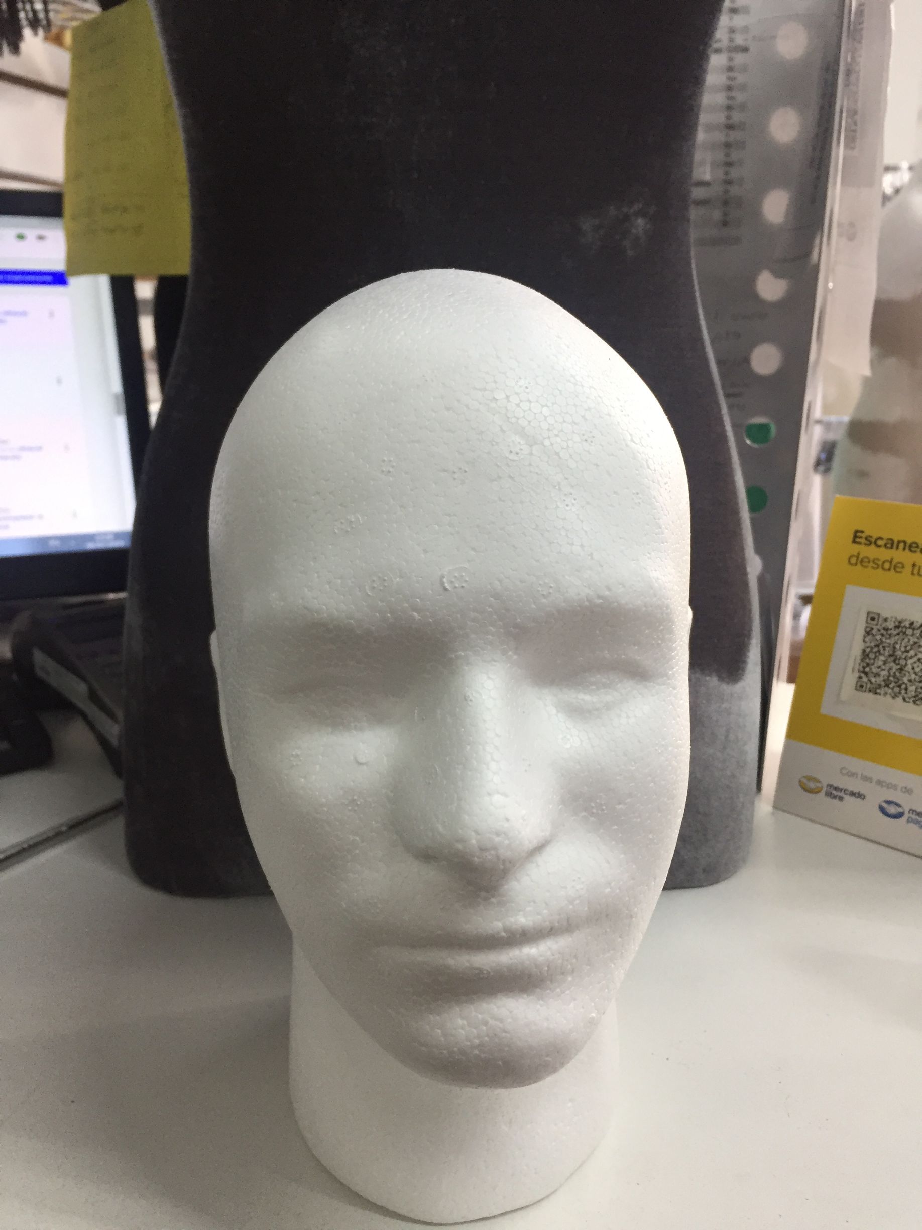 Cabeza de poliestireno blanco delante de un maniquí negro, entorno de oficina.