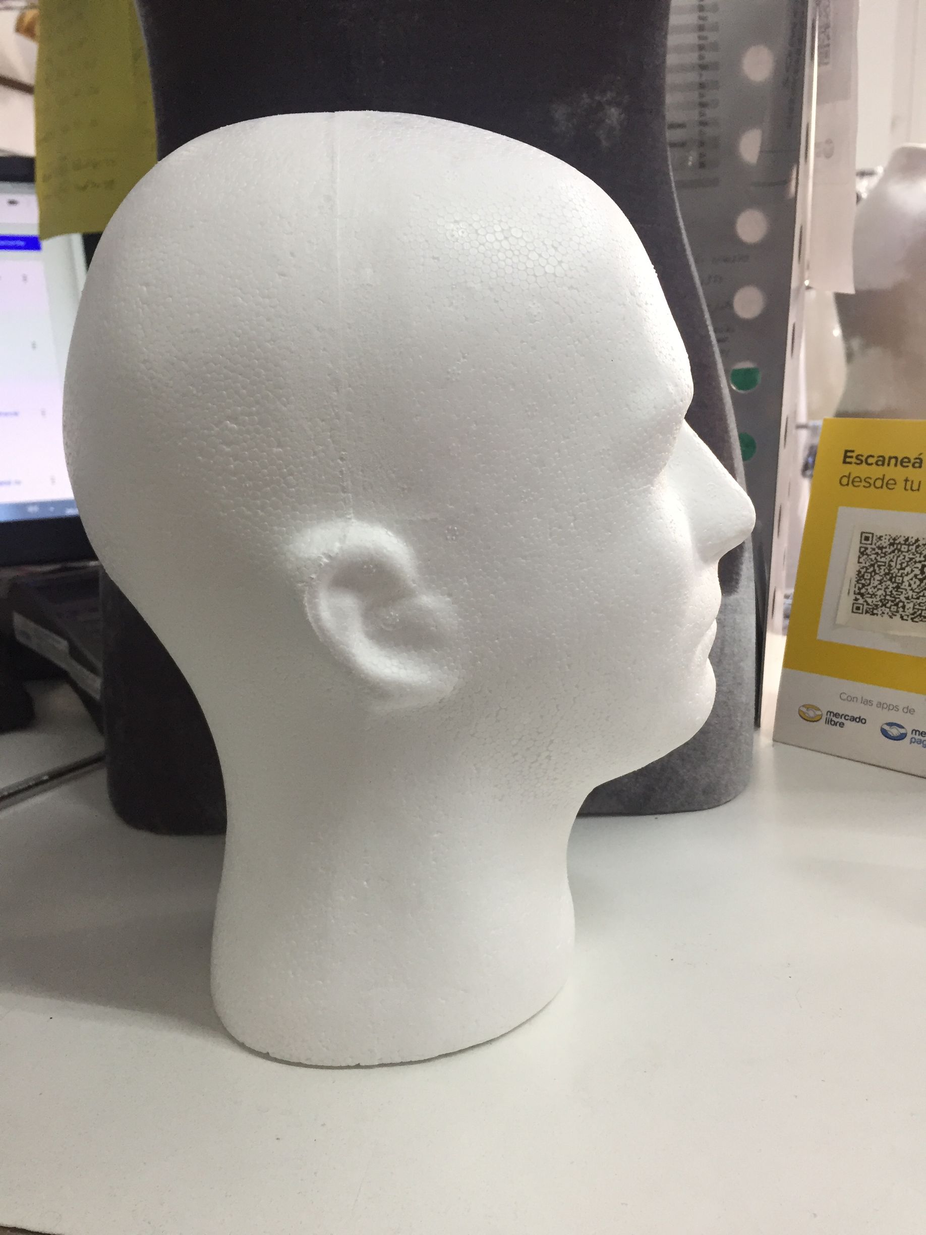 Cabeza de maniquí de poliestireno blanco sobre un escritorio, vista de perfil.