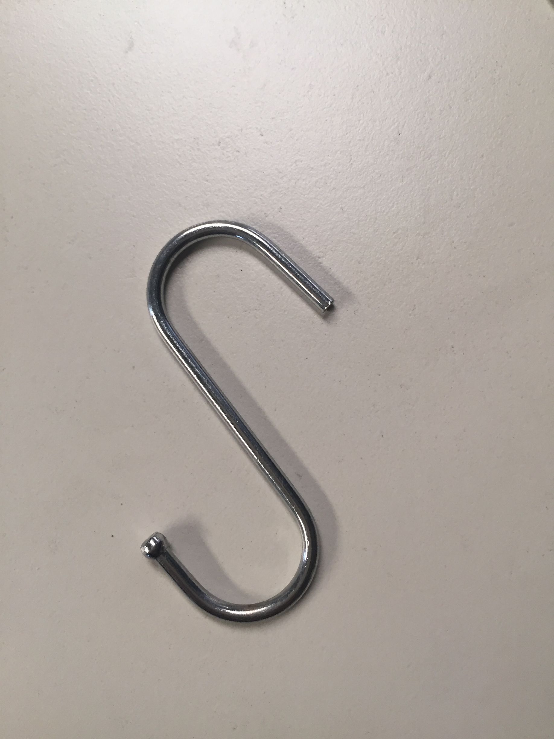 Gancho plateado en forma de S sobre superficie blanca.