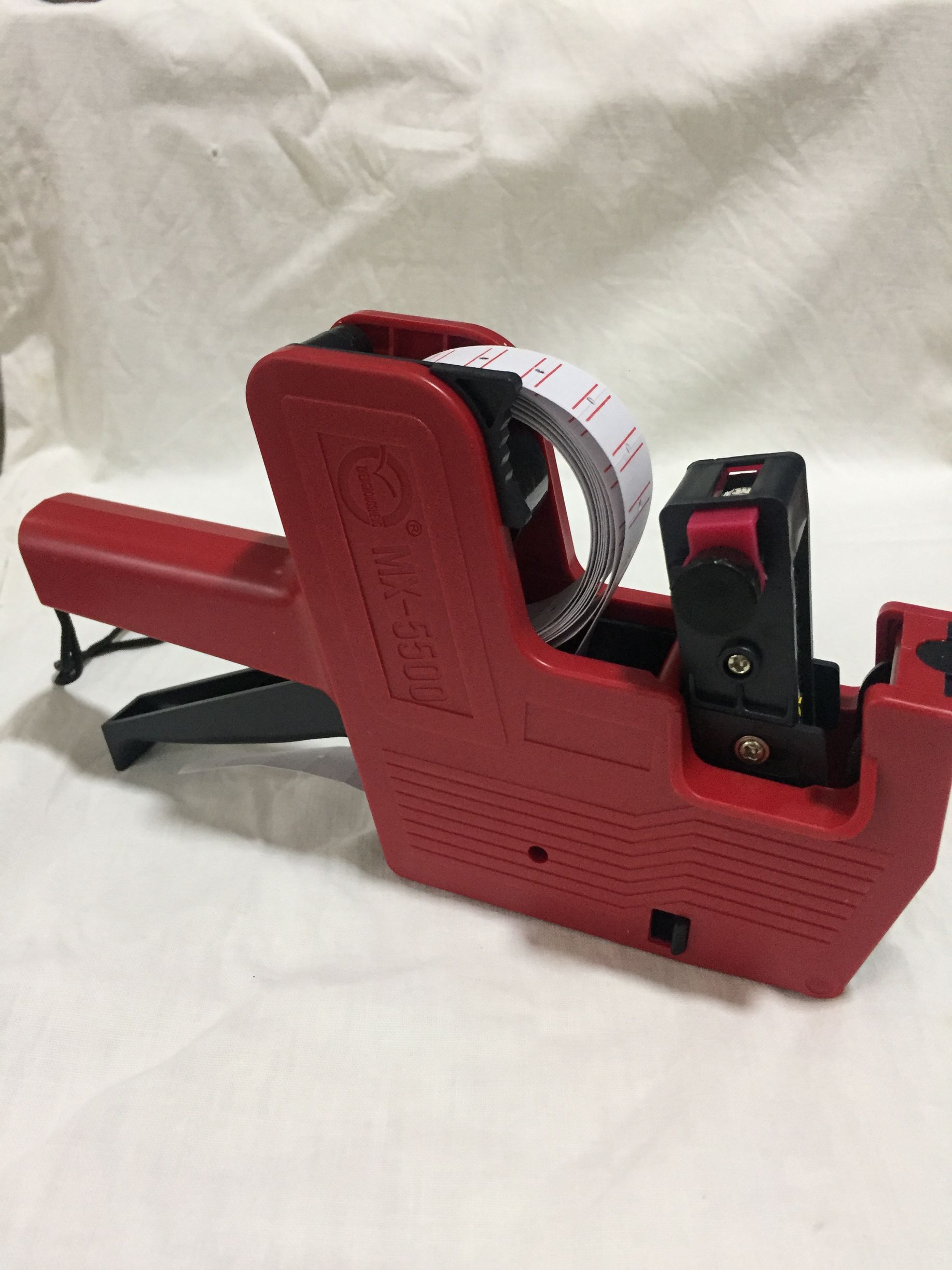 Máquina etiquetadora de precios de color rojo con etiquetas de precios de color blanco sobre una superficie blanca.