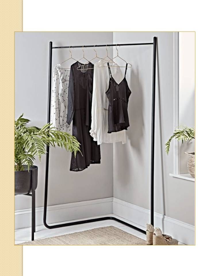 Perchero negro con prendas en un rincón de una habitación, plantas y suelo beige.