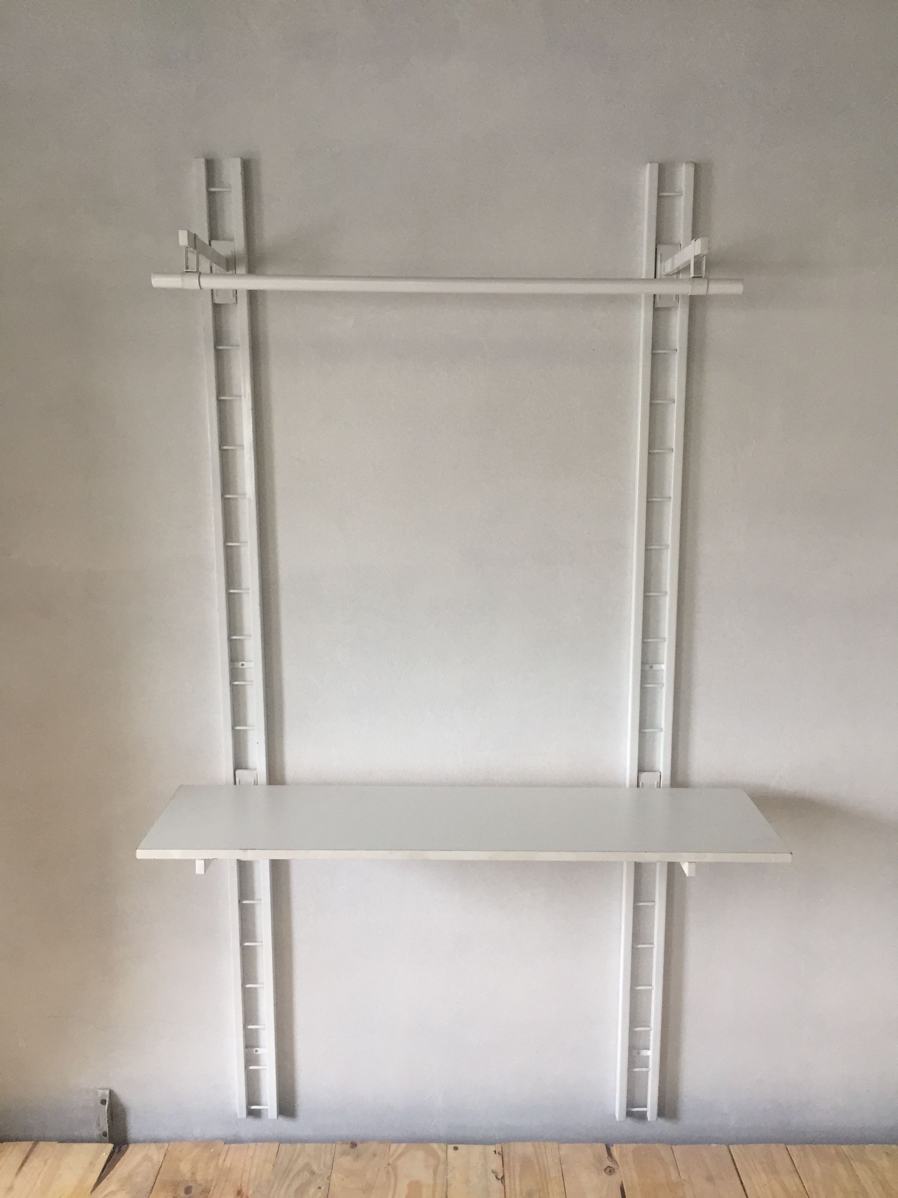 Estantería de pared de color blanco, con barra y estante, sobre una pared de color gris claro.