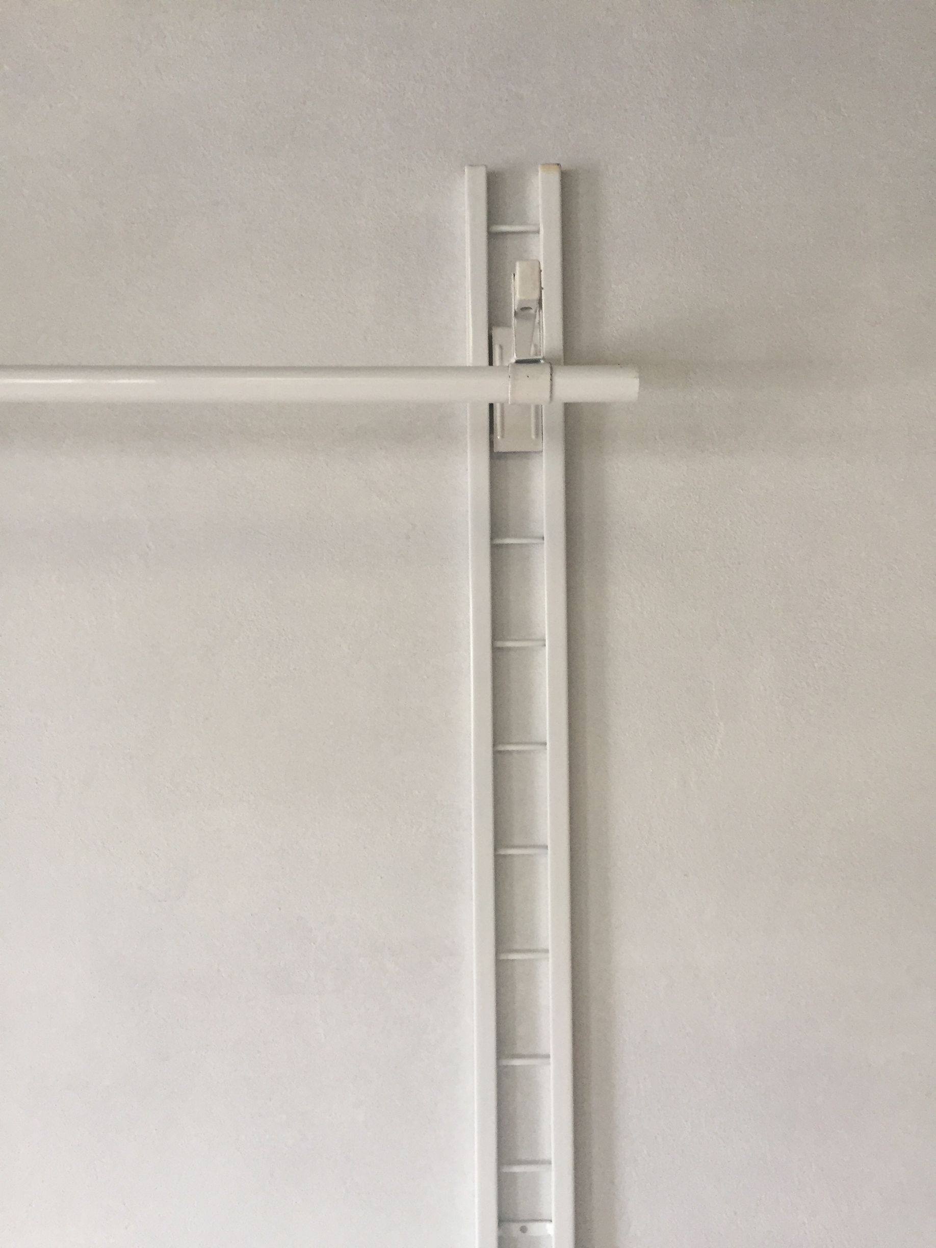 Barra de armario de color blanco fijada a una pared blanca con un riel vertical y un soporte de apoyo.